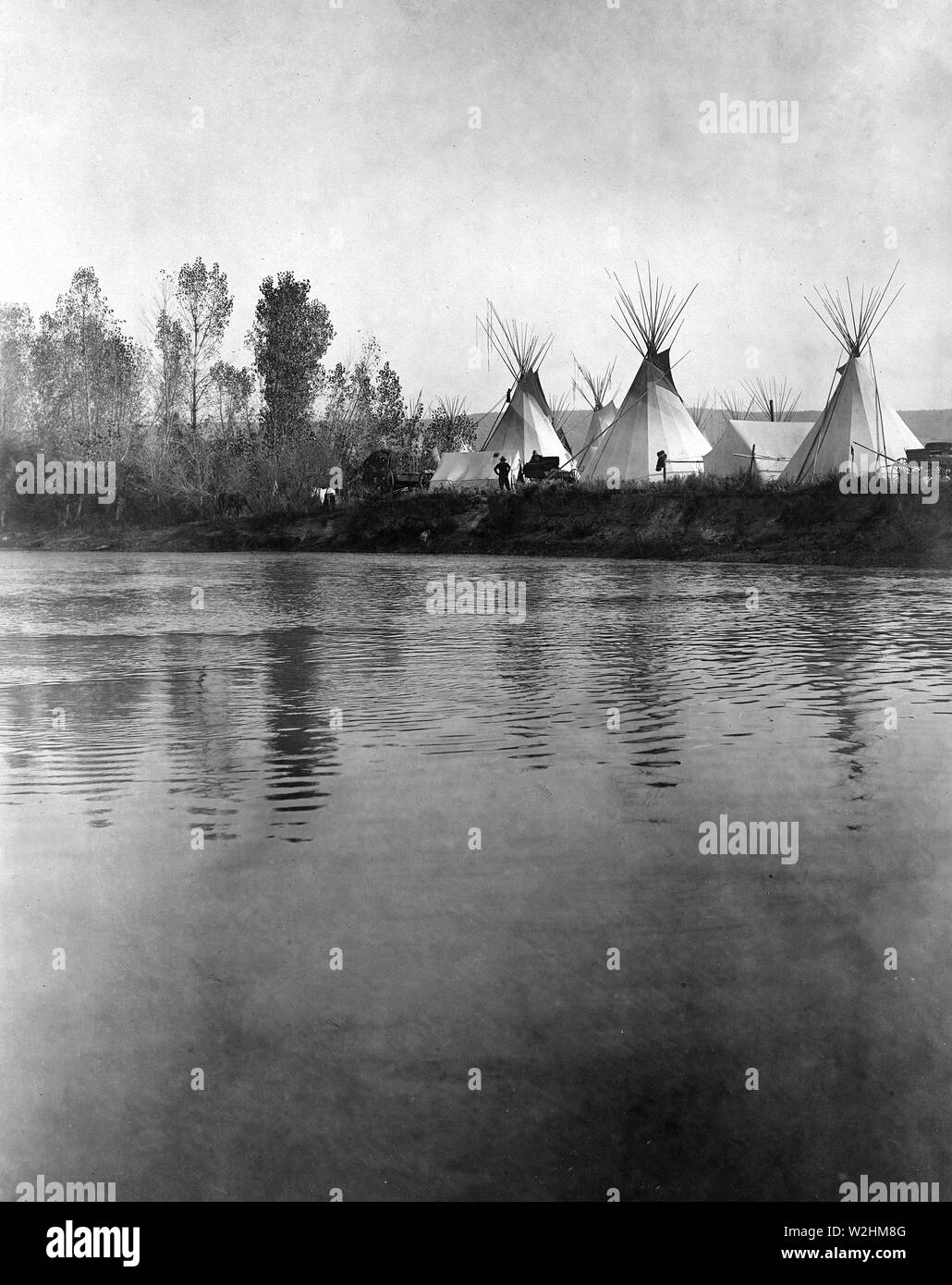 Edward S. Curtis indiens des États-Unis - campement Crow avec tipis, tentes, les charrettes, les chevaux et les hommes vus de la rive lointaine de la rivière ca. 1908 Banque D'Images Edward S. Curtis indiens des États-Unis - campement Crow avec tipis, tentes, les charrettes, les chevaux et les hommes vus de la rive lointaine de la rivière ca. 1908 Banque D'Images