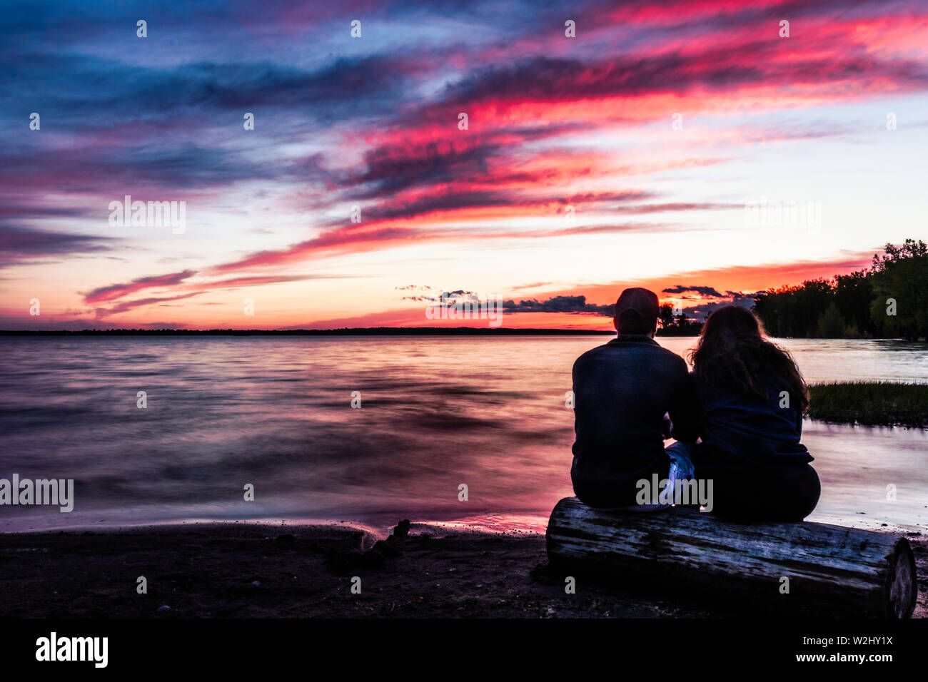 Couple assis sur une plage à admirer le coucher du soleil Banque D'Images
