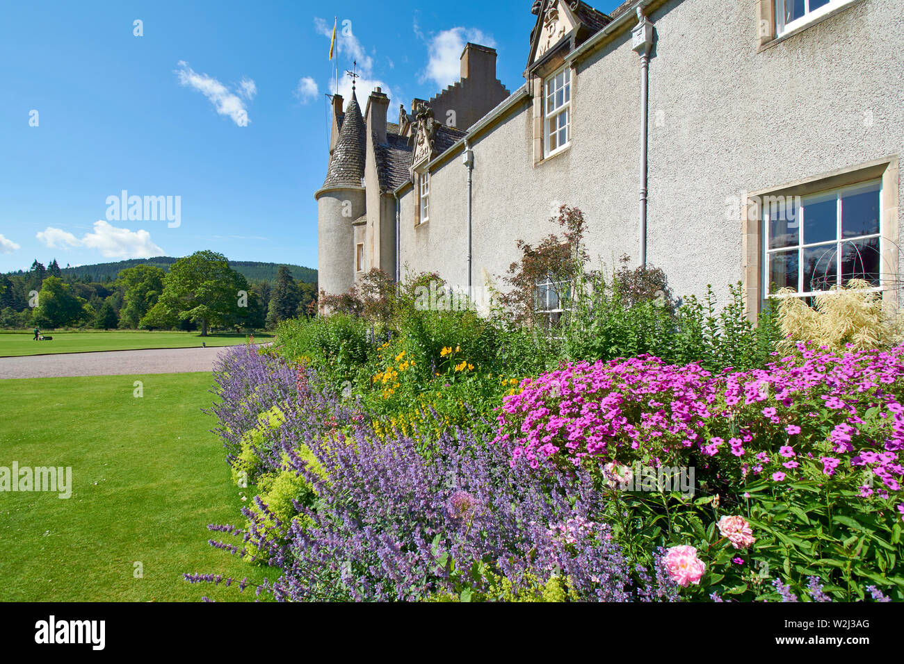 BALLINDALLOCH CHÂTEAU ET JARDINS BANFFSHIRE ECOSSE EN ÉTÉ LA FLEUR SUPERBE FRONTIÈRE ET MAN MOWING THE LAWN Banque D'Images