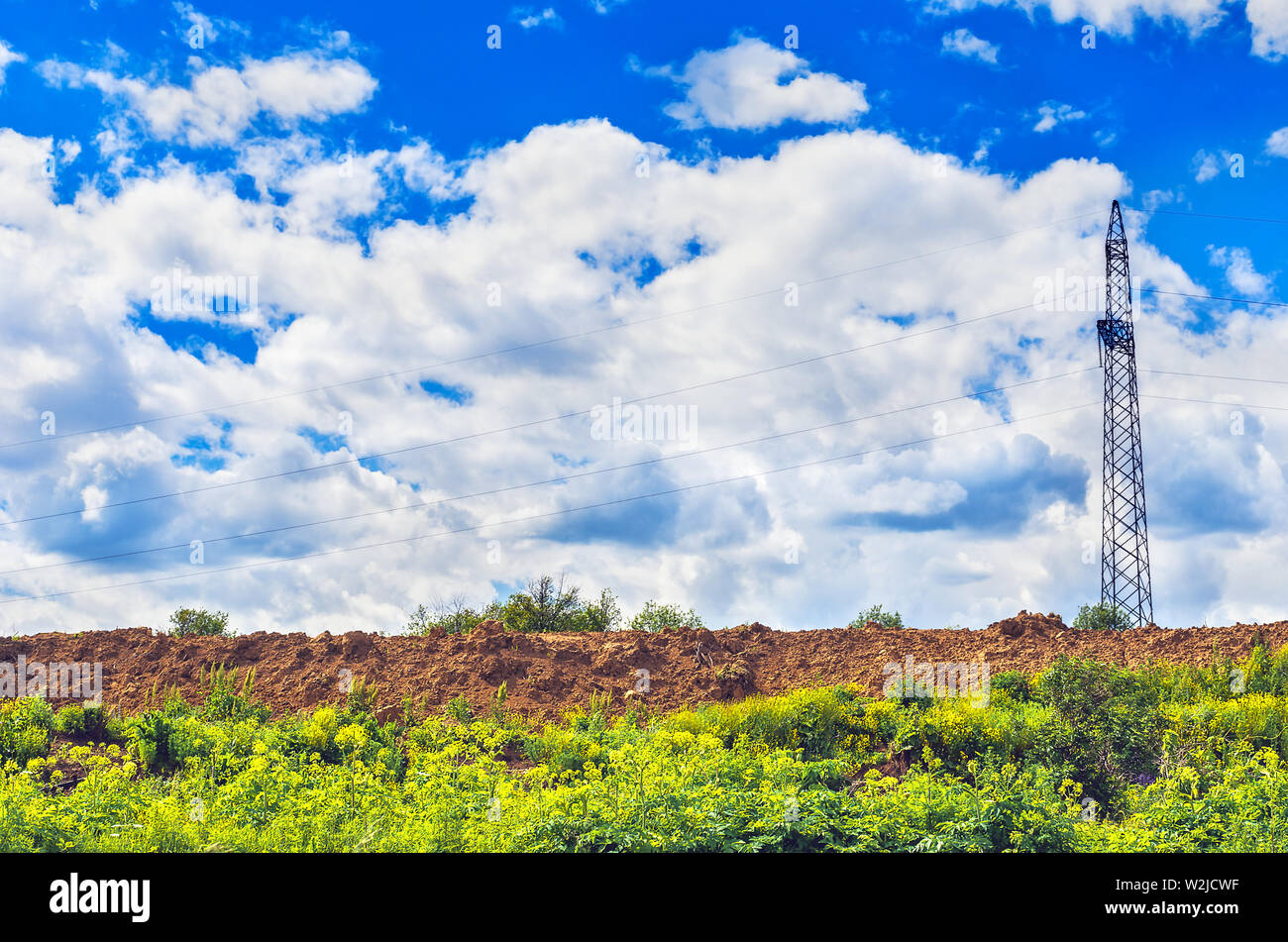Tour de la ligne d'alimentation en métal, de la construction du sol du site Heap, et des nuages sur la végétation d'été Ciel bleu sur une journée ensoleillée. Banque D'Images