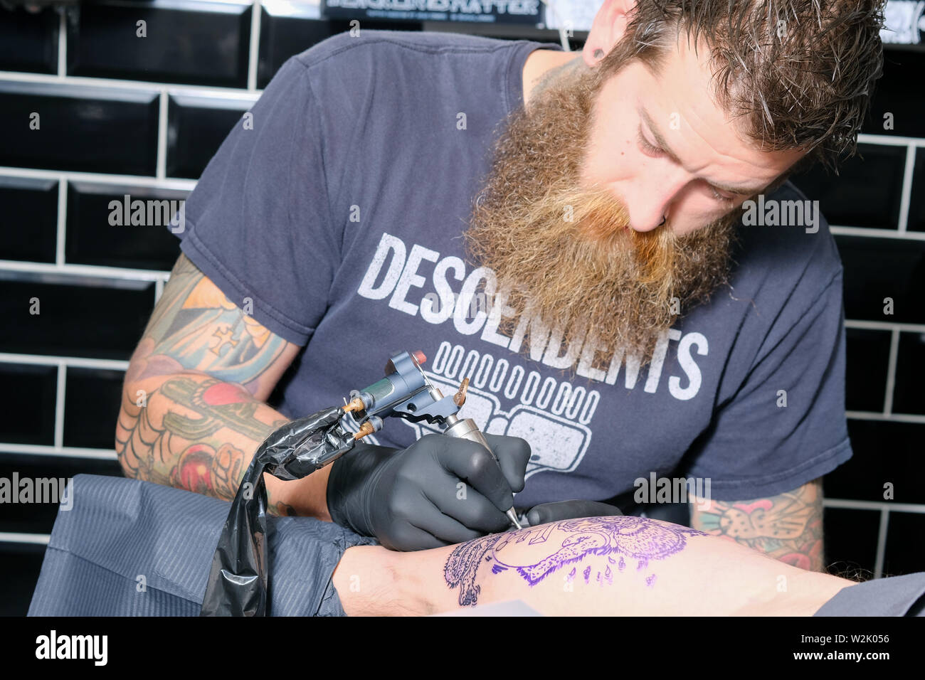 Un tatoueur ou tatoueur travaille sur un client Créer un tatouage ou un morceau de body art en utilisant une machine à tatouer électrique. Banque D'Images Un tatoueur ou tatoueur travaille sur un client Créer un tatouage ou un morceau de body art en utilisant une machine à tatouer électrique. Banque D'Images