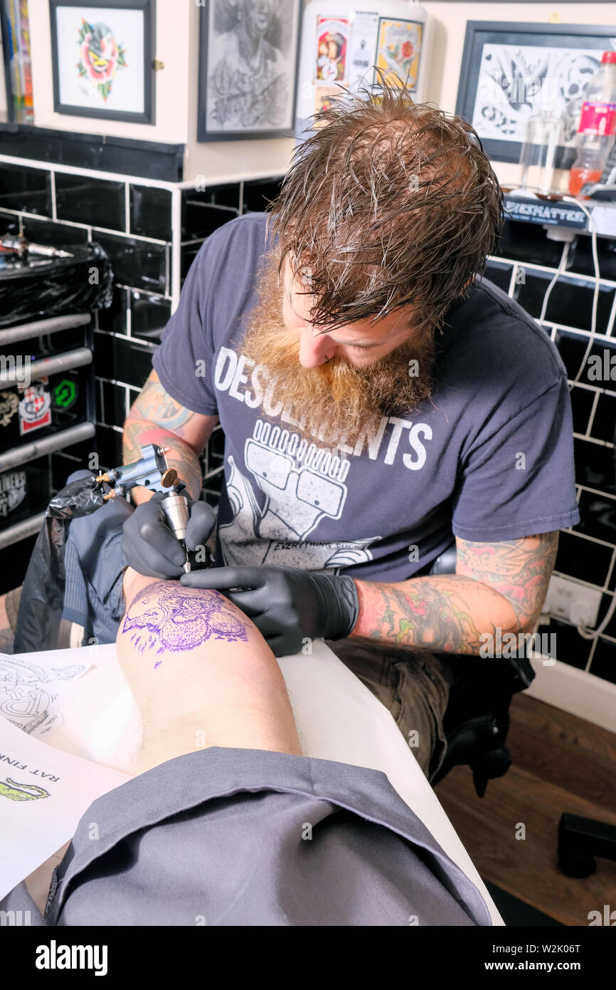Un tatoueur ou tatoueur travaille sur un client Créer un tatouage ou un morceau de body art en utilisant une machine à tatouer électrique. Banque D'Images