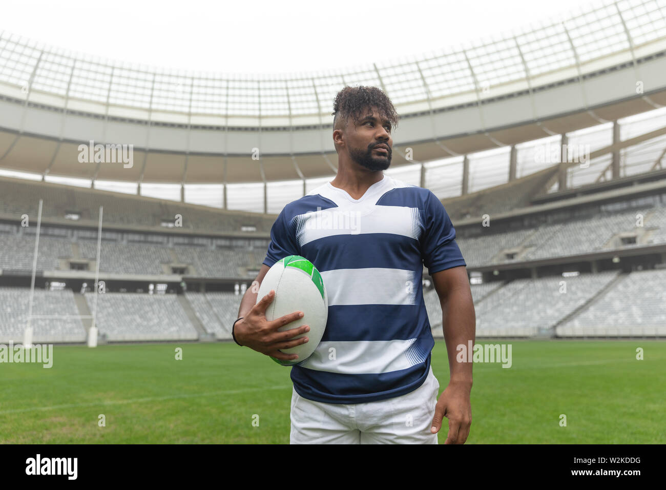 African American rugby player debout avec ballon de rugby et à l'écart dans le stade Banque D'Images