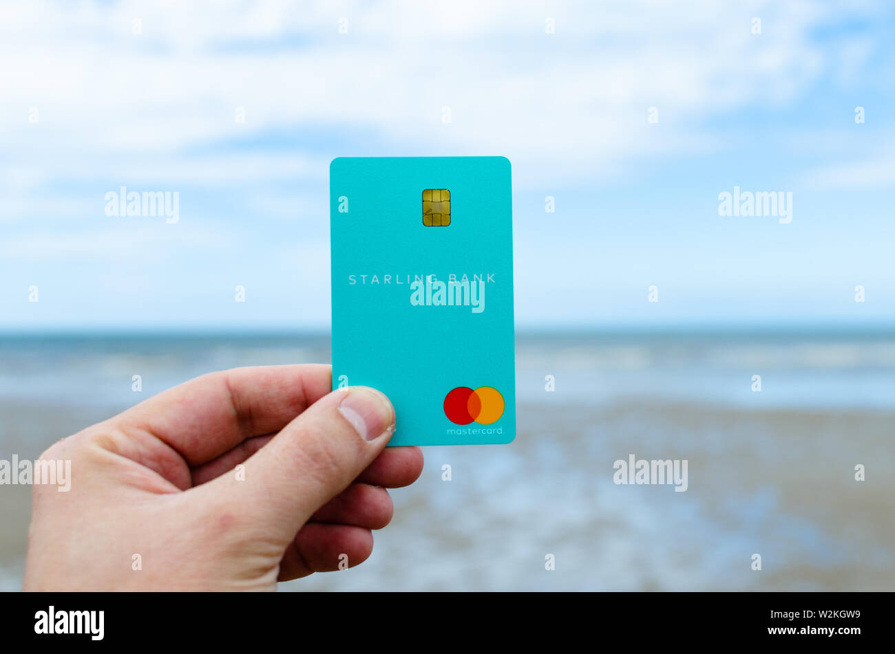 Carte bancaire Starling tenir la main avec l'arrière-plan flou seashore. Banque D'Images