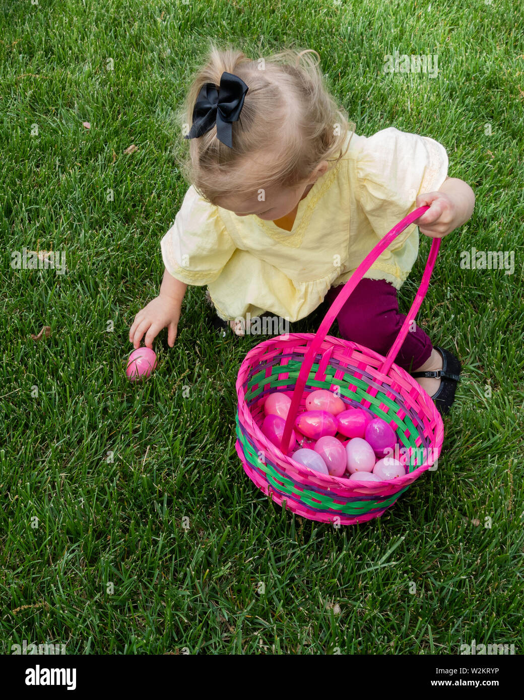 Deux ans caucasien blond-haired girl picking up un oeuf de Pâques en plastique à mettre dans son panier. Banque D'Images