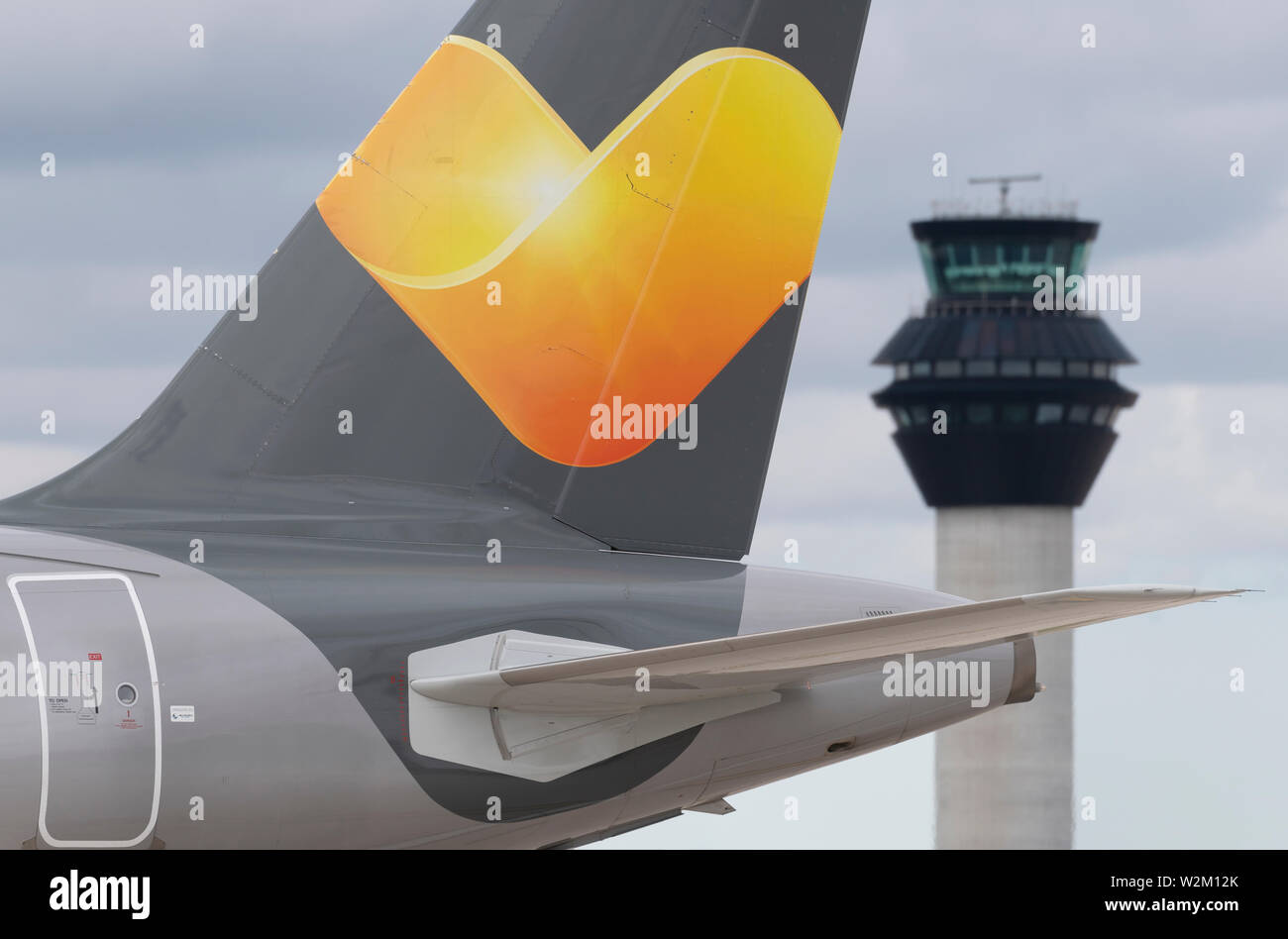 La tailfin d'un avion de Thomas Cook au sol le long de la piste en face de la tour de contrôle à l'aéroport de Manchester. Banque D'Images