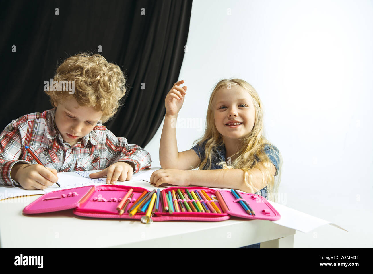 Garçon et fille se préparer à l'école après une longue pause de l'été. Retour à l'école. Peu de modèles de race blanche dimensions ensemble sur fond noir et blanc. L'enfance, l'éducation, les devoirs de vacances ou concept. Banque D'Images