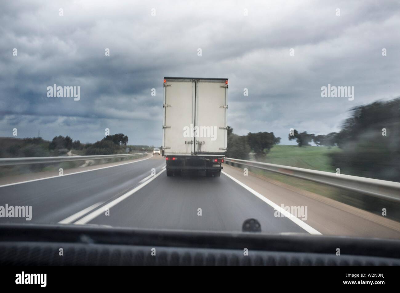 Derrière la conduite de camion lent sur la route un jour de pluie. Vue depuis l'intérieur de la voiture. Flou de mouvement. Banque D'Images