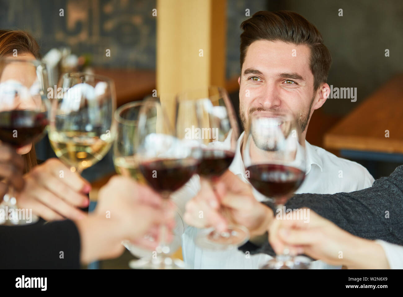 Young man toasting avec un verre de vin avec des amis au restaurant Banque D'Images