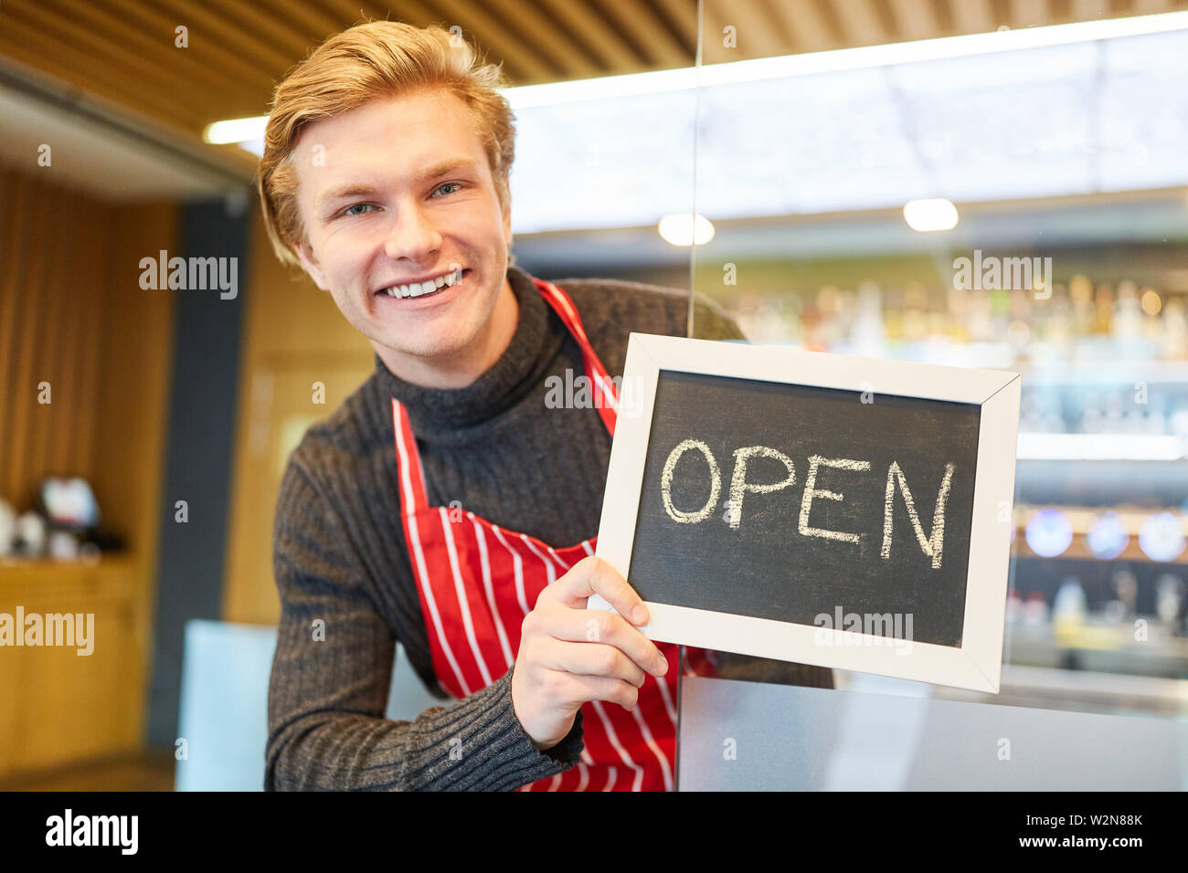 Jeune homme qu'un restaurant fondateur montre un tableau avec le lettrage Ouvrir Banque D'Images