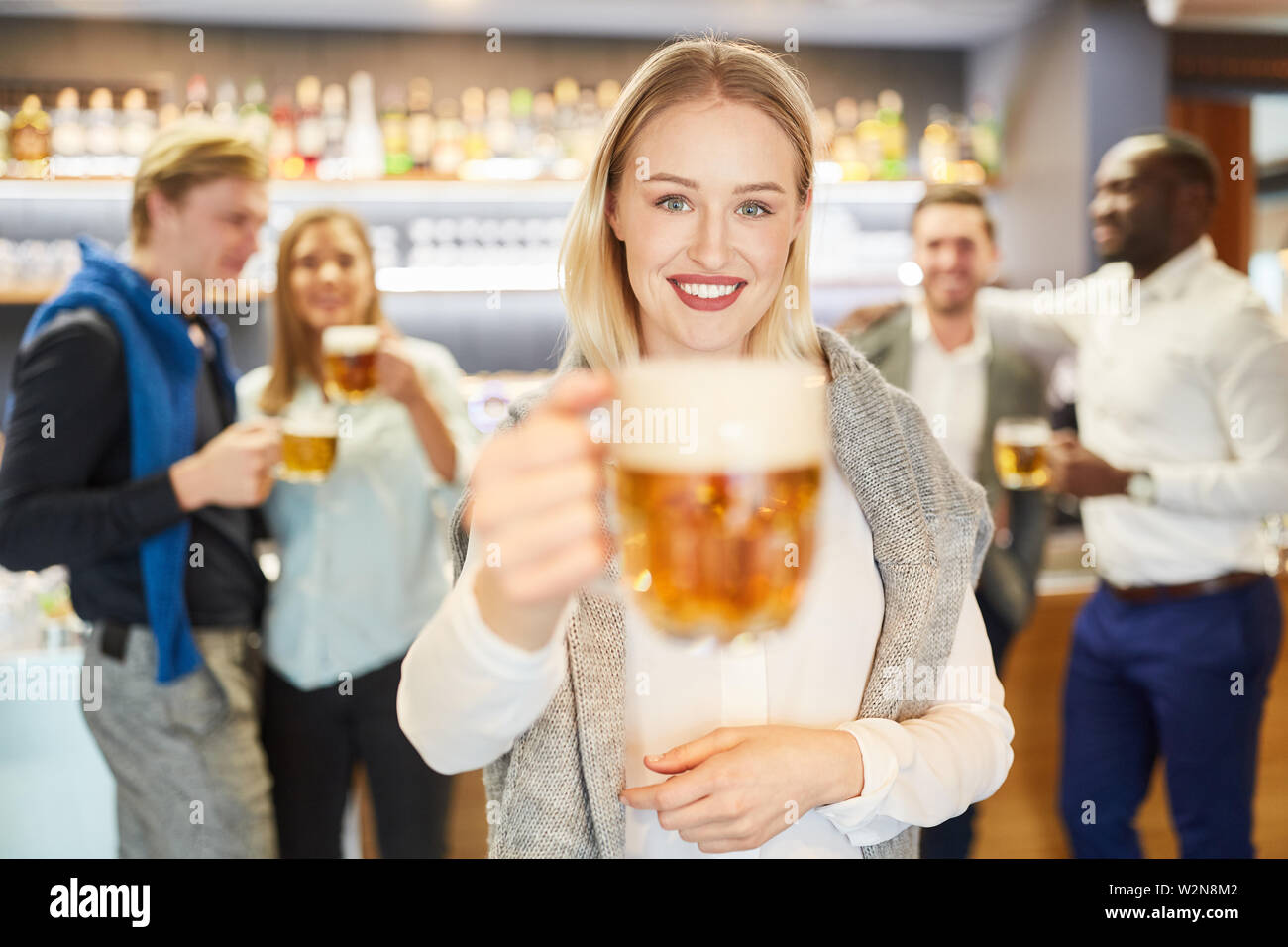 Toasts à la jeune femme à la caméra dans un pub avec des amis dans l'arrière-plan Banque D'Images