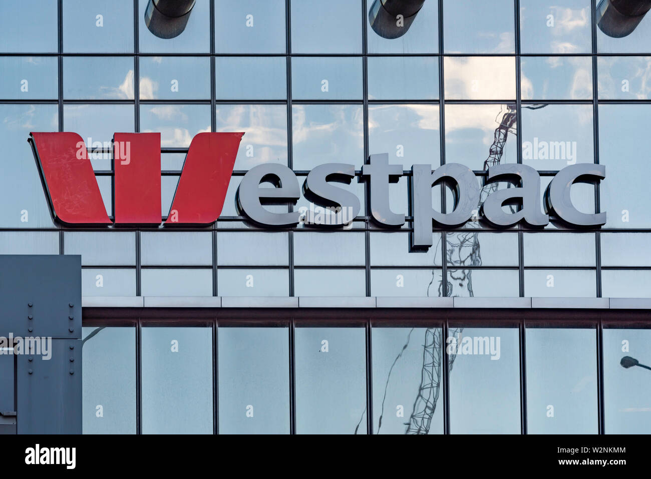 Le logo et le nom de la banque australienne Westpac sur l'extérieur d'un édifice de verre avec la réflexion d'une grue et nuages dans l'arrière-plan Banque D'Images
