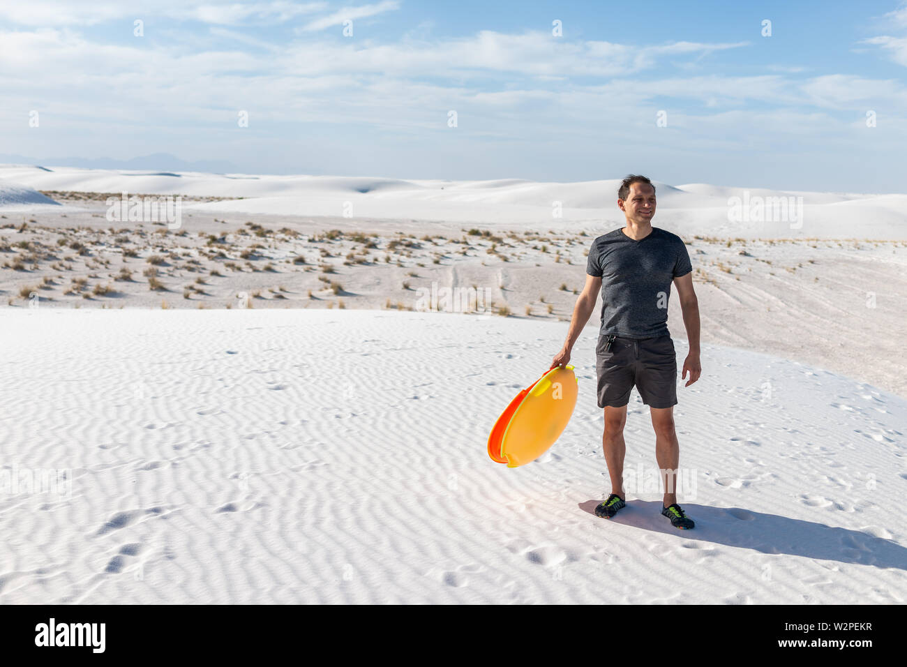 Homme heureux sur du sable dans les dunes de sable blanc national monument au Nouveau Mexique holding disque coloré pour traîneau glissant sur hills Banque D'Images