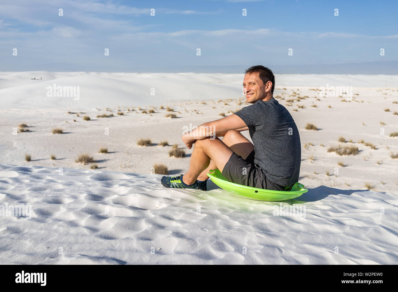 Heureux homme assis sur le sable en dunes de sable blanc national monument au Nouveau Mexique sur disque vert pour traîneau glissant sur hills Banque D'Images
