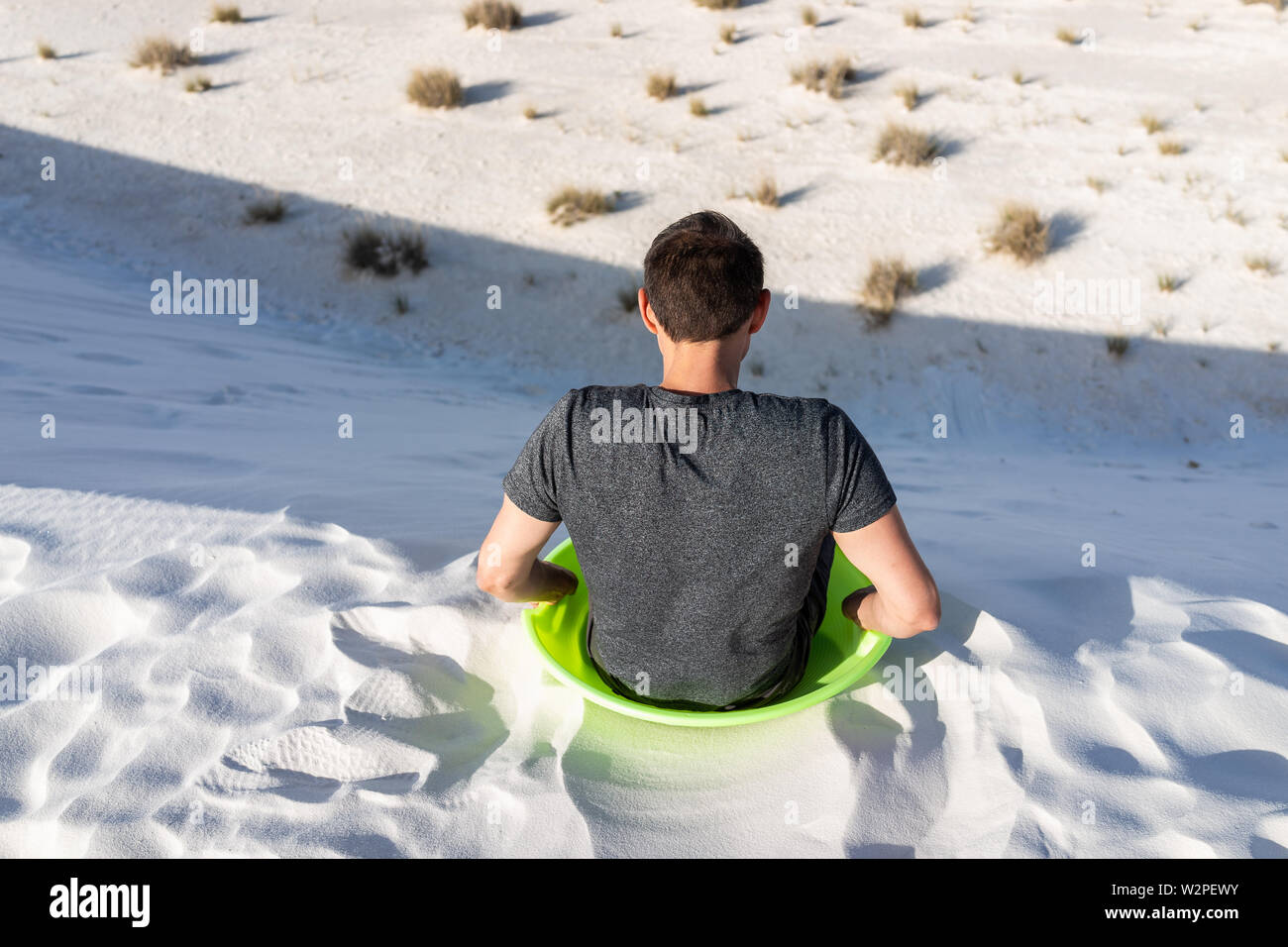 Retour de l'homme assis sur le sable en dunes de sable blanc national monument au Nouveau Mexique sur disque vert pour traîneau glissant sur hills Banque D'Images