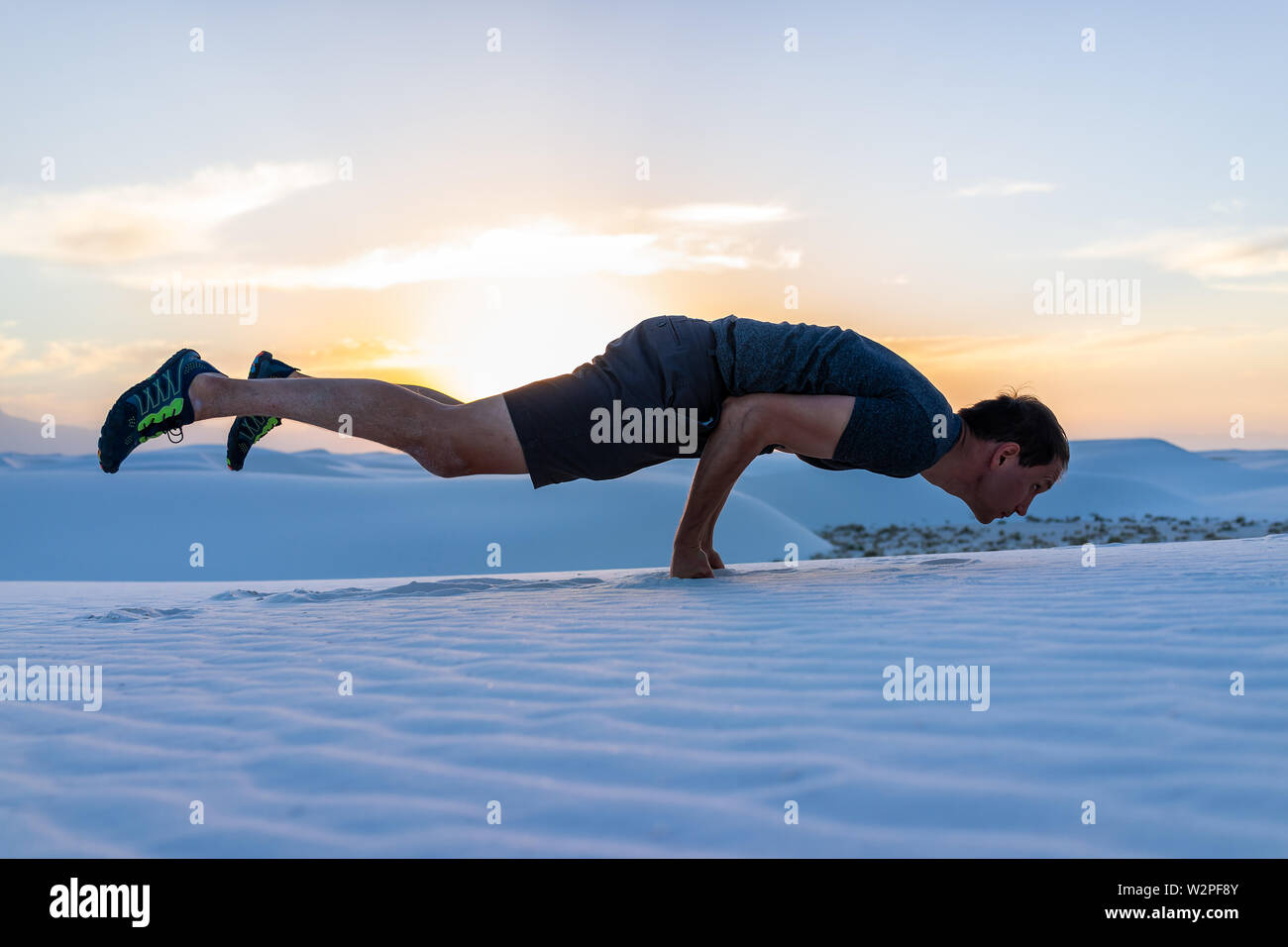 L'exercice de l'homme faisant l'exercice du plateau en équilibre sur les poings dans les dunes de sable blanc monument national en vue du Nouveau Mexique de coucher du soleil Banque D'Images