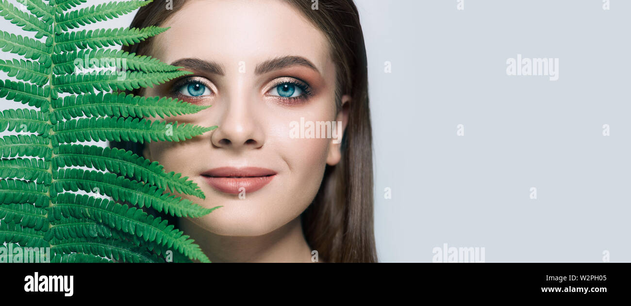 Beau portrait de femme aux yeux bleus et verts usine près de visage. Cosmétique Biologique Banque D'Images