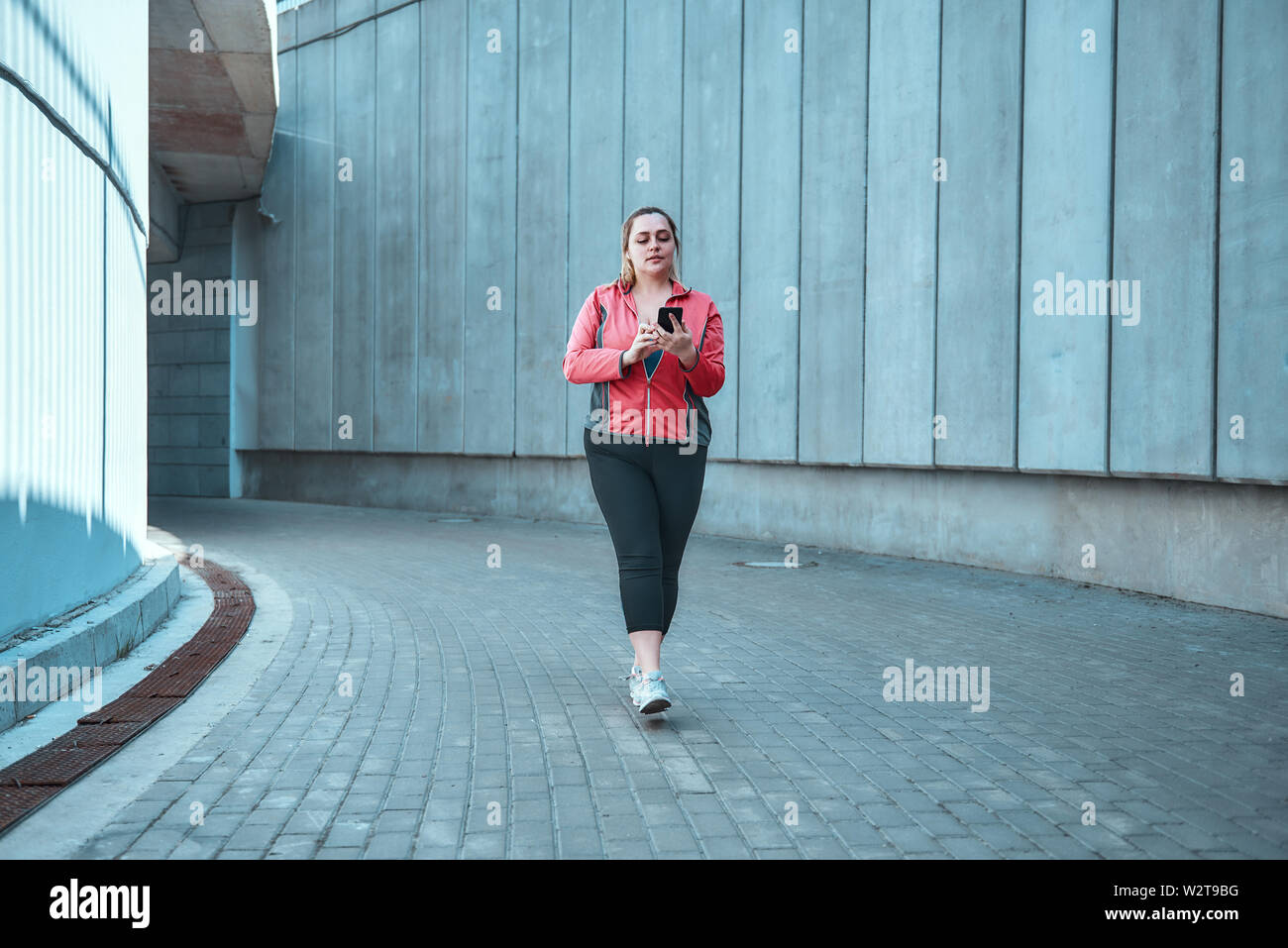 Prêt pour l'entraînement. Les jeunes grande taille femme sur les sports clothes holding smart phone en se tenant debout à l'extérieur. Les technologies numériques. Sport concept Banque D'Images