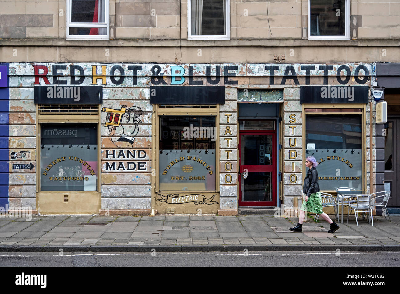 Une jeune femme marche par Red Hot & Blue Tattoo shop à Brougham Street, Édimbourg, Écosse, Royaume-Uni. Banque D'Images