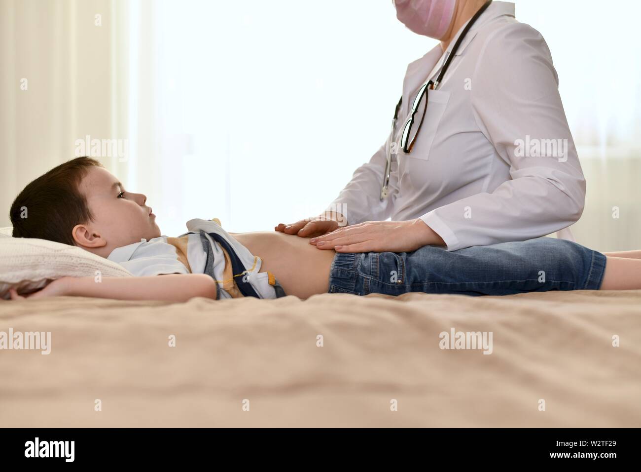 Le Medecin Examine Le Ventre D Un Enfant Malade A La Maison Un Garcon Avec Un Visage Serieux Triste Est Allonge Sur Le Lit Et En Regardant Le Stethoscope Sur Son Cou Photo Le Medecin Examine Le Ventre D Un Enfant Malade A La Maison Un Garcon Avec Un Visage Serieux Triste Est Allonge Sur Le Lit Et En Regardant Le Stethoscope Sur Son Cou Photo