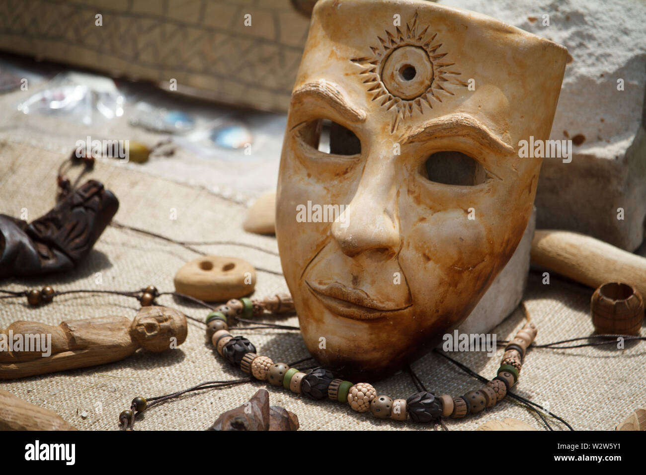 Un réaliste beige masque de papier mâché avec symbole de soleil sur le front en branches d'arbre vert Banque D'Images