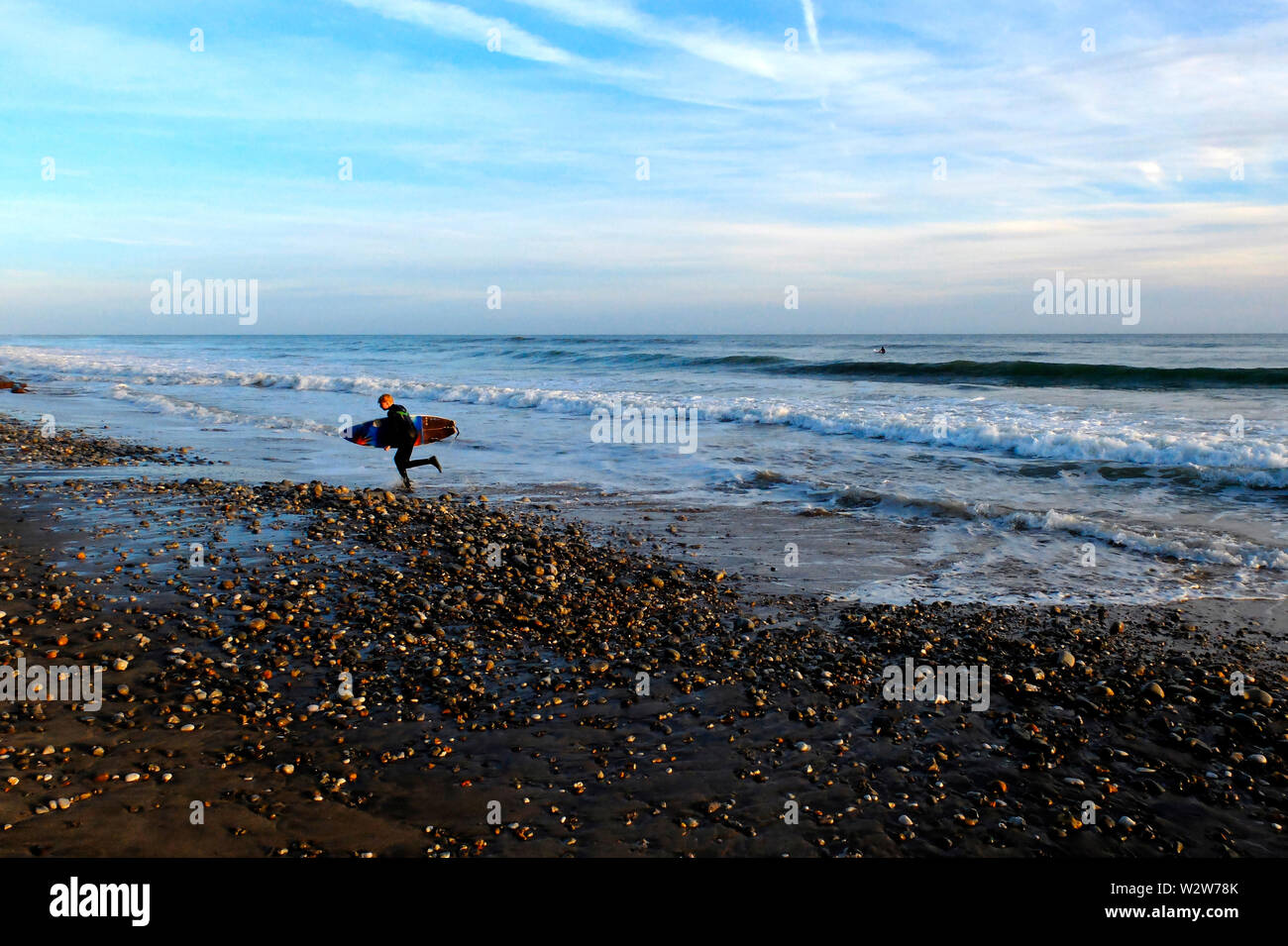 Un jeune homme qui court hors de la mer portant sa planche de surf sous le bras à Compton Chine, Compton Bay, île de Wight Banque D'Images