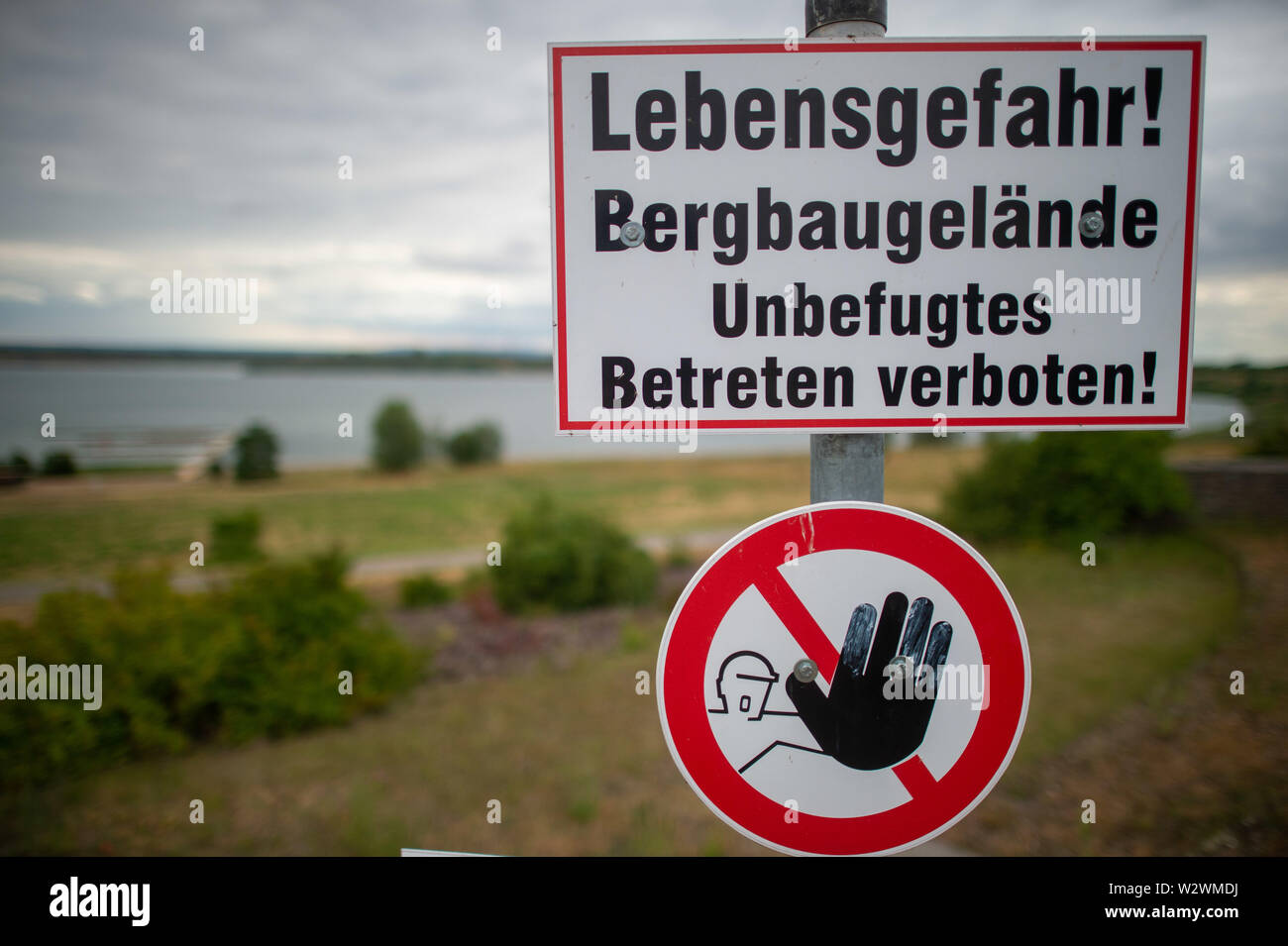 09 juillet 2019, la Saxe-Anhalt, Schadeleben : "attention à la vie ! Site de construction de montagne - aucune intrusion' est écrit sur un panneau d'avertissement placé en face de la rive du lac Concordias. Autour de dix ans après le gigantesque glissement de Nachterstedt, la population locale et les clients pourront se baigner encore une fois sur la rive nord du lac de l'Université Concordia du 13 juillet 2019. Le 18 juillet 2009, plusieurs millions de mètres cubes de sol avait glissé dans le lac créé par une ancienne mine de lignite à ciel ouvert. Plusieurs maisons sont tombés dans les profondeurs, trois résidents sont morts. Depuis l'accident, le lac a été fermé pendant toute l'utilisation touristique. Ph Banque D'Images