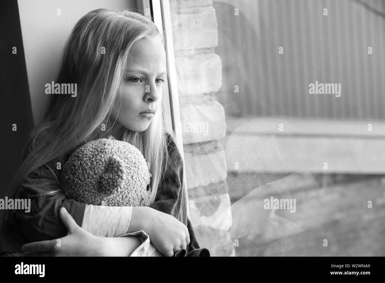 Petite fille sans-abri avec ours assis sur le rebord de fenêtre Banque D'Images