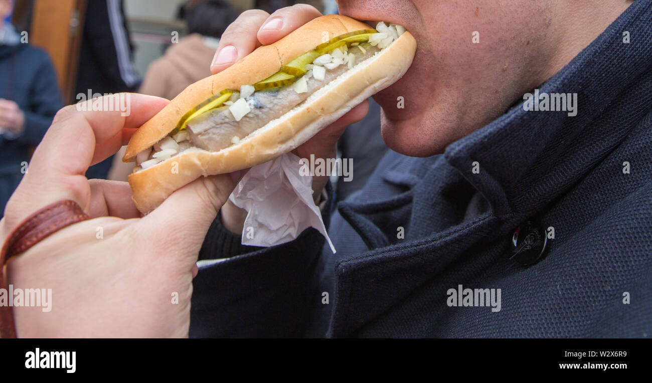 Man eating burgers de fruits de mer dans une rue avec le hareng, oignon et pickle Banque D'Images