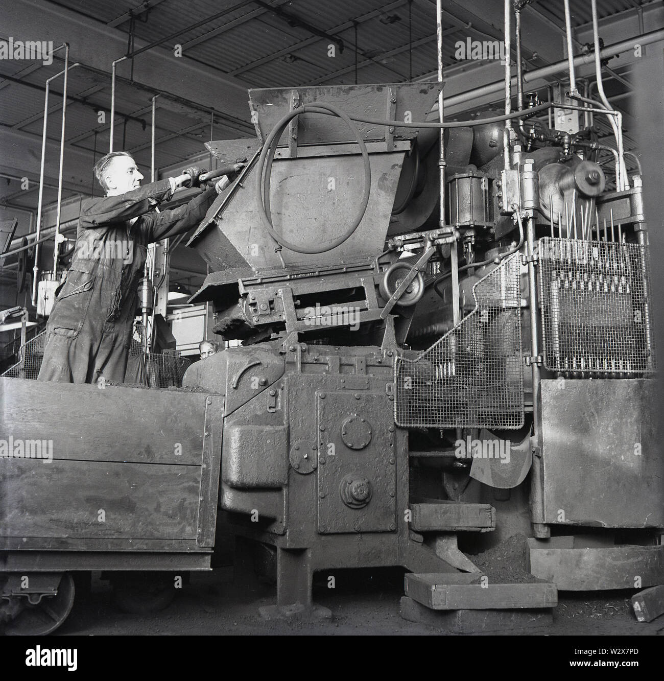 Années 1950, historique, un travailleur dans des combinaisons à l'aide de machines à l'usine de batteries toujours prêt à Walthamstow, London, England, UK. L'usine a produit carbone-zinc qui ont été les premiers commerical piles sèches. Banque D'Images
