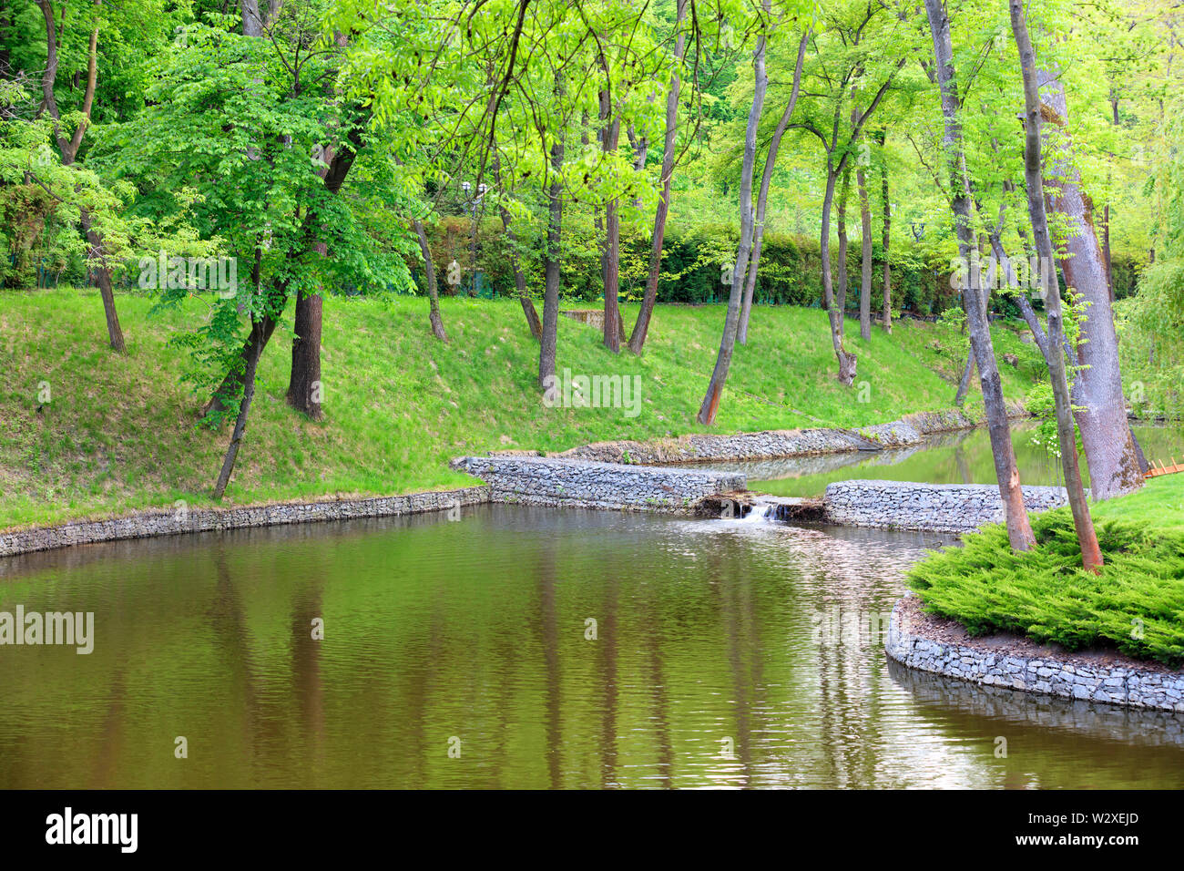 Une forêt lac avec une cascade d'eau de trop-plein dans un magnifique parc est situé entre les divers arbres à feuilles caduques, encadré sur les rives de l'cobblest connecté Banque D'Images