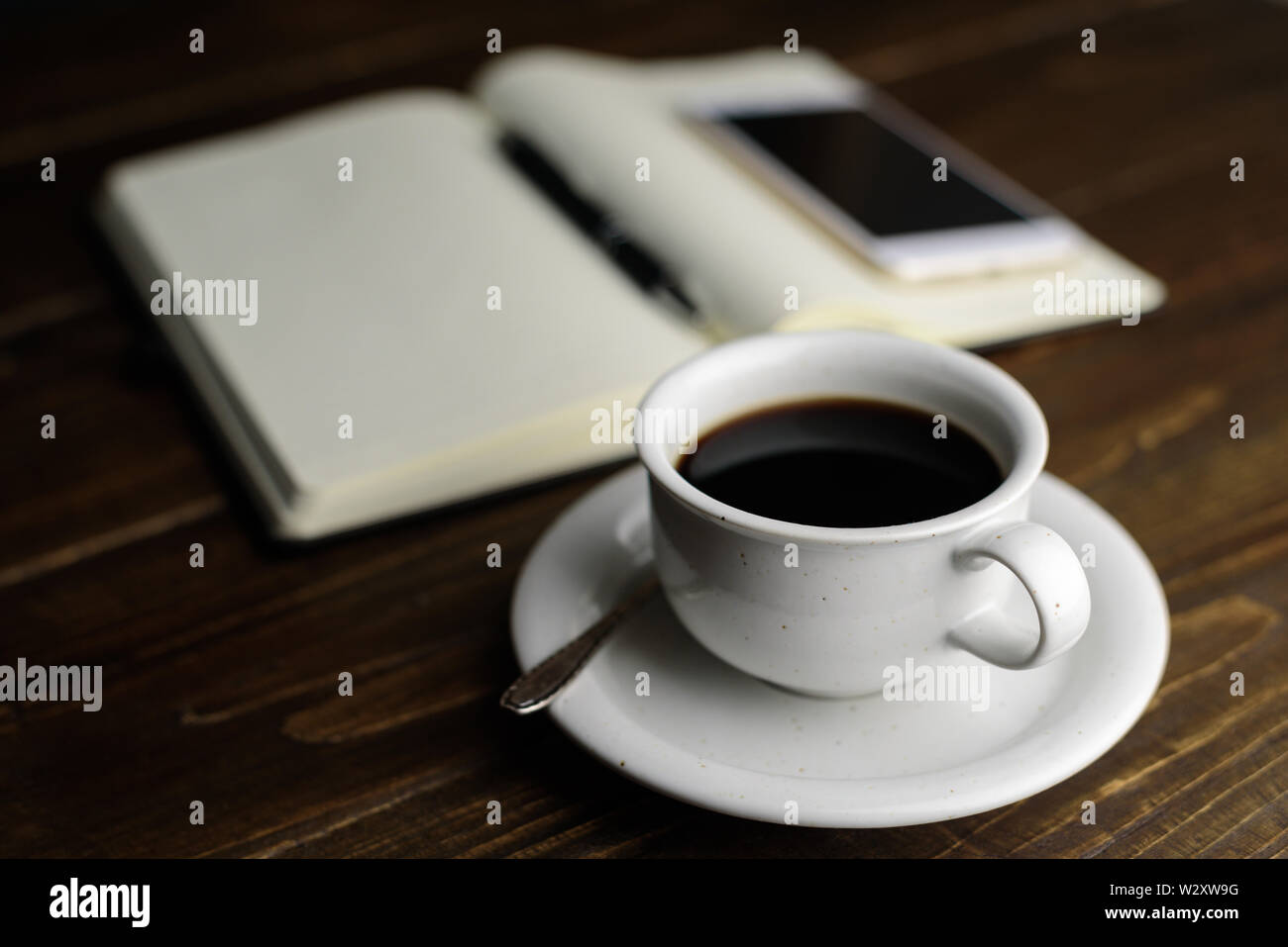 Café noir, stylo et ordinateur portable sur une table en bois sombre. Lieu de travail Banque D'Images