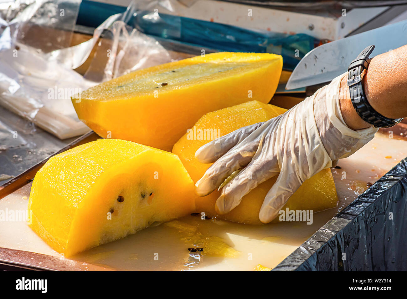 Main tenant la pastèque jaune et utiliser un couteau pour couper un morceau. Banque D'Images