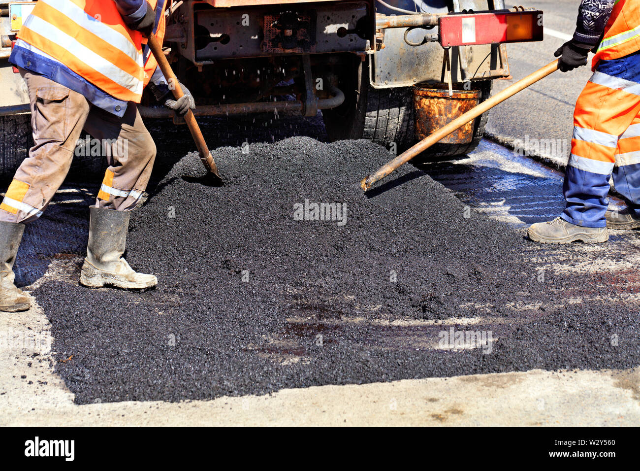 Le groupe de travail des travailleurs de la route met à jour la partie de la route avec de l'asphalte chaud avec des pelles et la répartit uniformément sur la surface. Banque D'Images