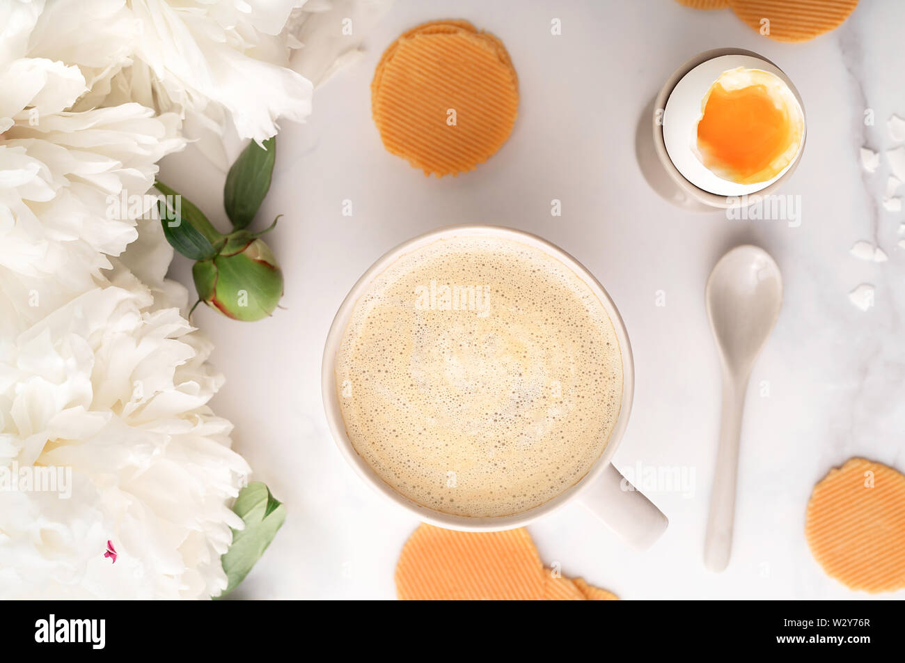 Vue de dessus de l'oeuf dur doux avec liquide jaune orange en céramique egg cup, tasse de café avec cuillère en céramique mince et croustillante, les croustilles de maïs et belle pivoine blanche. Le petit-déjeuner gratuit. Mise à plat. Banque D'Images