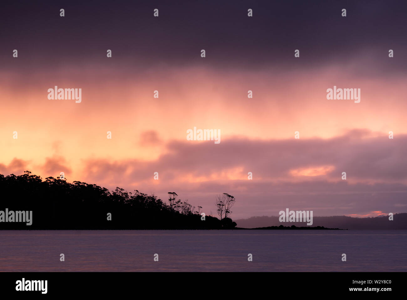 Nuageux et soleil colorés plus Norfolkbay avec silhouette d'arbres et de l'île, Taranna, Tasmanie, Australie Banque D'Images