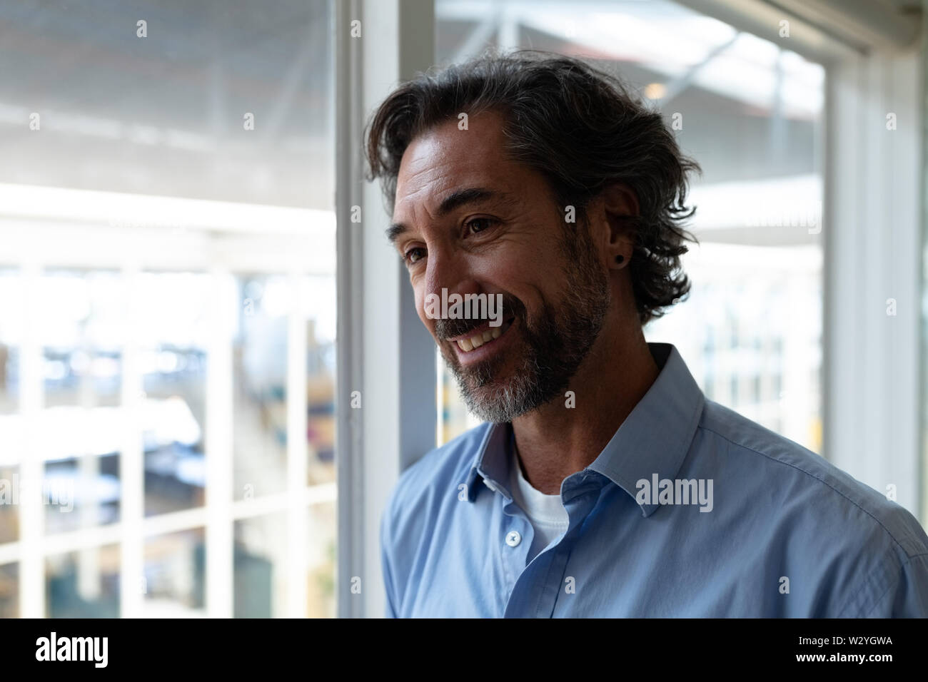 Happy businessman looking away while standing near window in office Banque D'Images