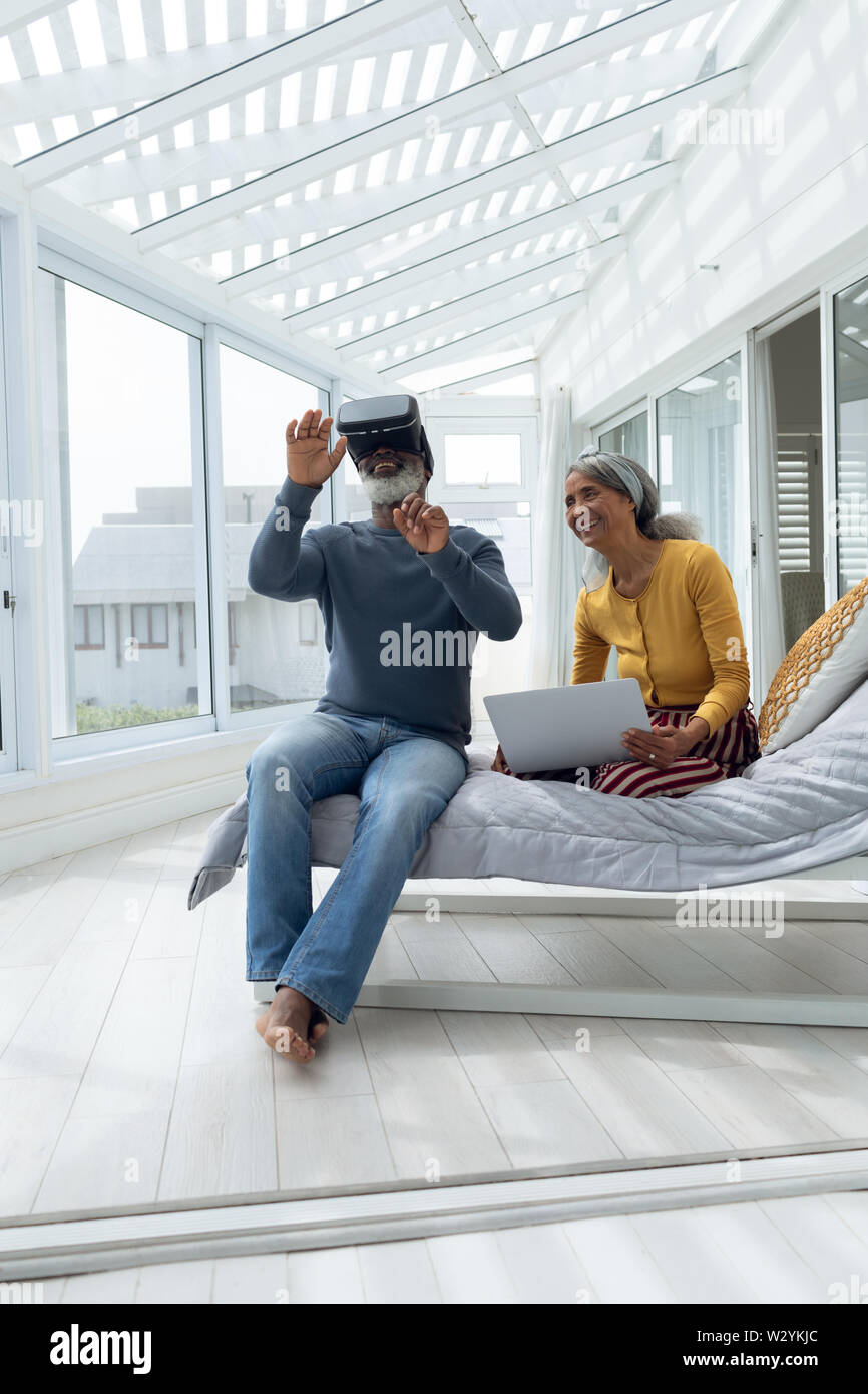 Couple assis sur un lit pendant l'utilisation de dispositifs numériques Banque D'Images