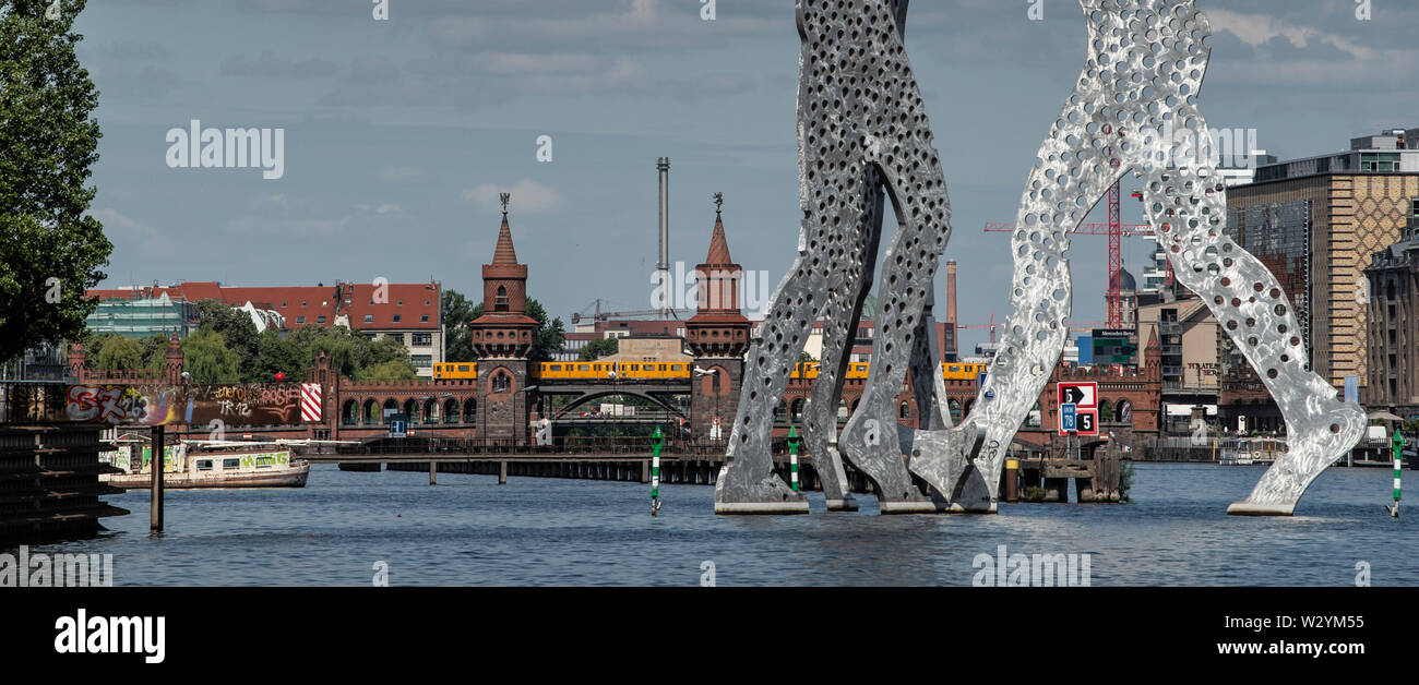 Berlin, Allemagne. 11 juillet, 2019. Un train traverse le pont Oberbaumbrücke. Il se trouve en face de l'homme par la molécule de sculpture sculpteur américain Jonathan Borofsky. Crédit : Paul Zinken/dpa/Alamy Live News Banque D'Images