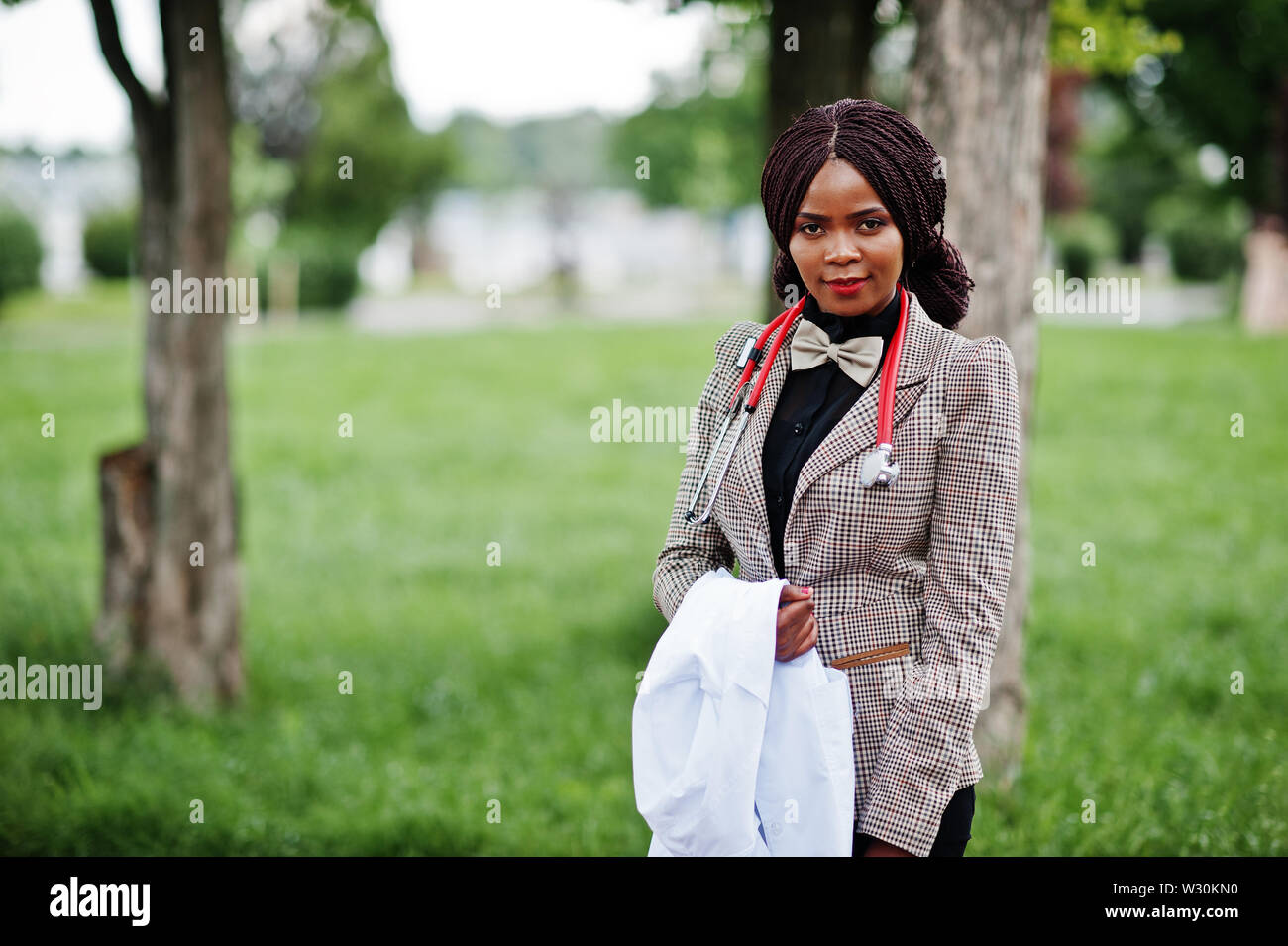 Young african american female doctor tenir manteau blanc sur la main avec un stéthoscope posé à l'extérieur. Banque D'Images
