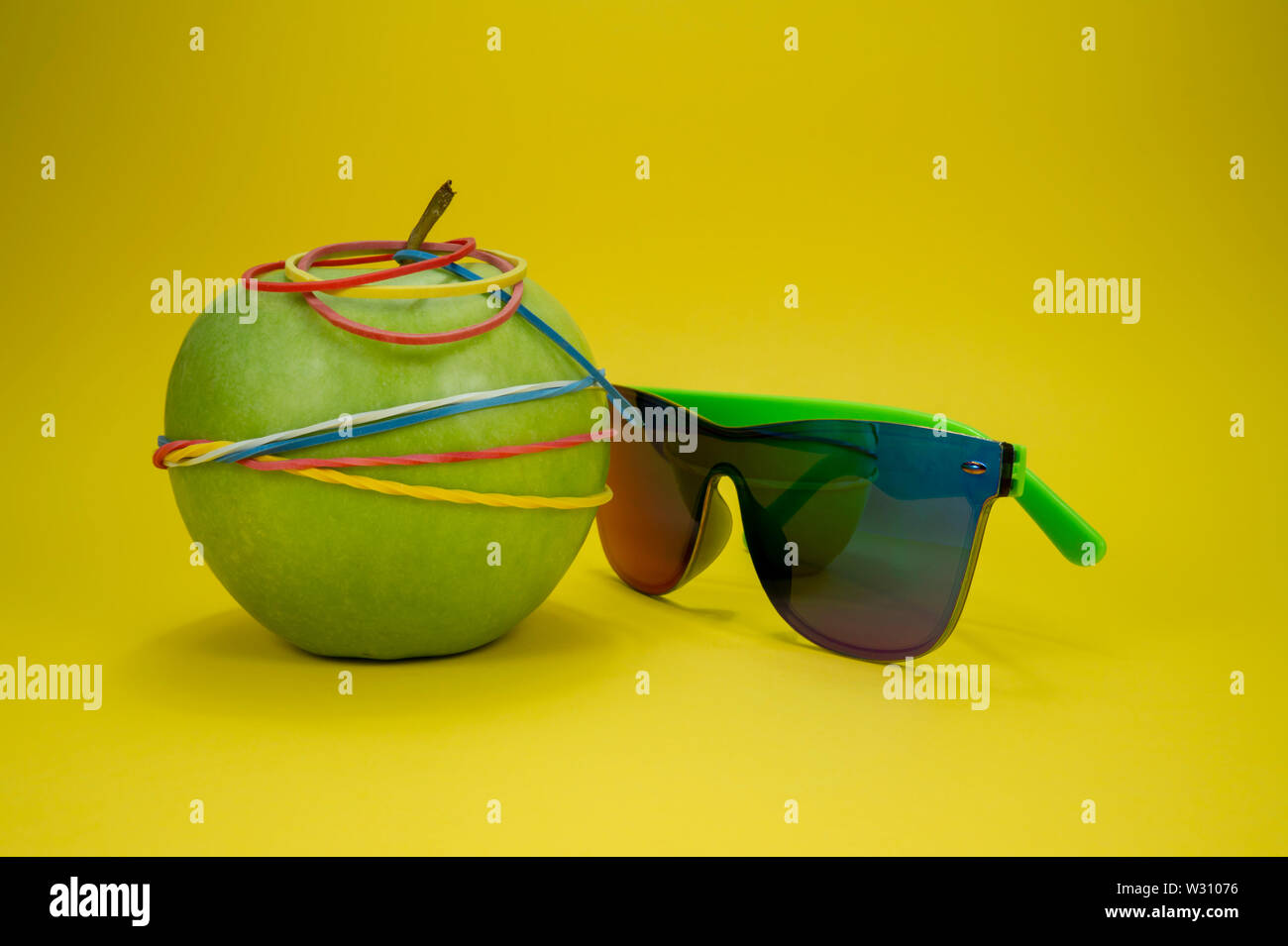 Green Apple lié aux bandes de caoutchouc et des lunettes de soleil de mode sur fond jaune. La simplicité à l'école ou l'alimentation, l'aerobic concept avec cop Banque D'Images