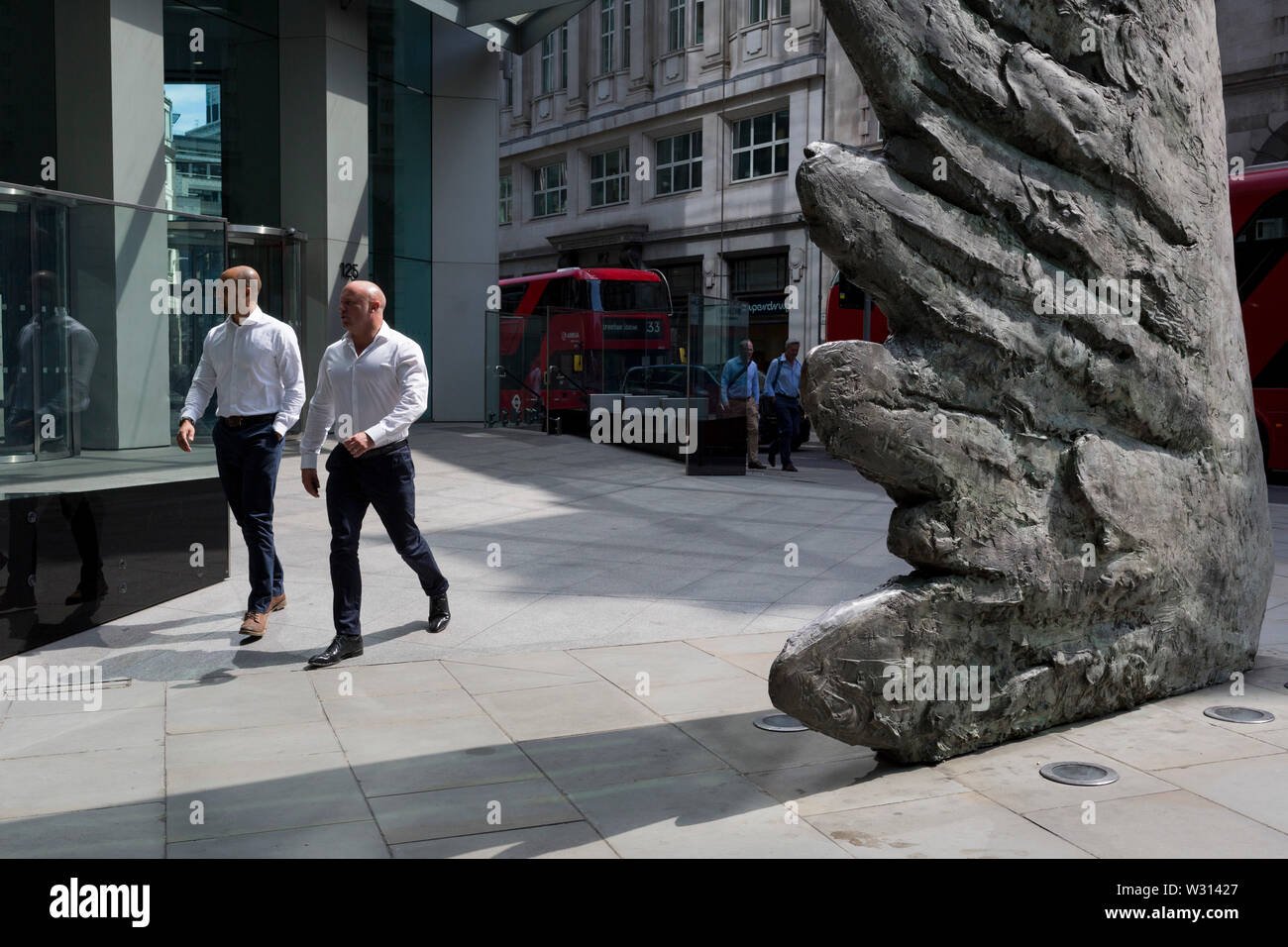 Les hommes d'affaires de l'industrie financière à pied au-delà de la sculpture intitulée City Wing sur Threadneedle Street dans la ville de Londres, le quartier financier de la capitale (aka le Square Mile), le 11 juillet 2019, à Londres, en Angleterre. L'aile est de la ville par l'artiste Christopher Le Brun. Les dix mètres de haut est la sculpture en bronze par le président de la Royal Academy of Arts, Christopher Le Brun, commandé par Hammerson en 2009. Elle est appelée 'La Ville' de l'aile et a été jeté par Morris Singer, fondateurs de l'art réputé pour être la plus ancienne fonderie d'art dans le monde. Banque D'Images