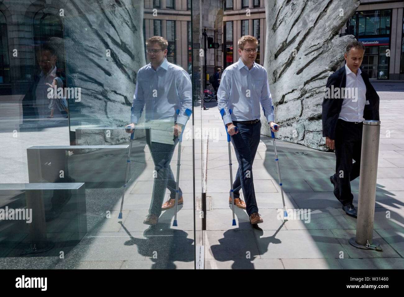 Les hommes d'affaires de l'industrie financière à pied au-delà de la sculpture intitulée City Wing sur Threadneedle Street dans la ville de Londres, le quartier financier de la capitale (aka le Square Mile), le 11 juillet 2019, à Londres, en Angleterre. L'aile est de la ville par l'artiste Christopher Le Brun. Les dix mètres de haut est la sculpture en bronze par le président de la Royal Academy of Arts, Christopher Le Brun, commandé par Hammerson en 2009. Elle est appelée 'La Ville' de l'aile et a été jeté par Morris Singer, fondateurs de l'art réputé pour être la plus ancienne fonderie d'art dans le monde. Banque D'Images