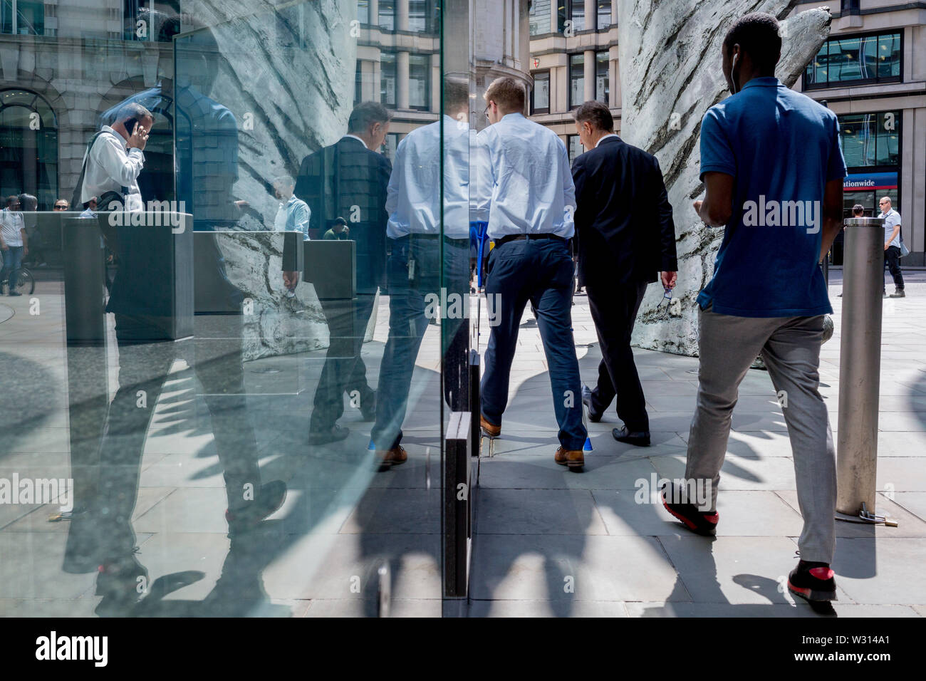 Les hommes d'affaires de l'industrie financière à pied au-delà de la sculpture intitulée City Wing sur Threadneedle Street dans la ville de Londres, le quartier financier de la capitale (aka le Square Mile), le 11 juillet 2019, à Londres, en Angleterre. L'aile est de la ville par l'artiste Christopher Le Brun. Les dix mètres de haut est la sculpture en bronze par le président de la Royal Academy of Arts, Christopher Le Brun, commandé par Hammerson en 2009. Elle est appelée 'La Ville' de l'aile et a été jeté par Morris Singer, fondateurs de l'art réputé pour être la plus ancienne fonderie d'art dans le monde. Banque D'Images