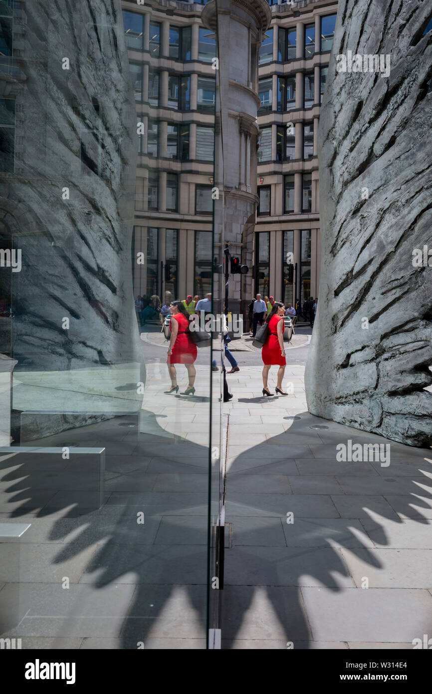 Une femme d'affaires de l'industrie financière en rouge passe devant la sculpture intitulée City Wing sur Threadneedle Street dans la ville de Londres, le quartier financier de la capitale (aka le Square Mile), le 11 juillet 2019, à Londres, en Angleterre. L'aile est de la ville par l'artiste Christopher Le Brun. Les dix mètres de haut est la sculpture en bronze par le président de la Royal Academy of Arts, Christopher Le Brun, commandé par Hammerson en 2009. Elle est appelée 'La Ville' de l'aile et a été jeté par Morris Singer, fondateurs de l'art réputé pour être la plus ancienne fonderie d'art dans le monde. Banque D'Images