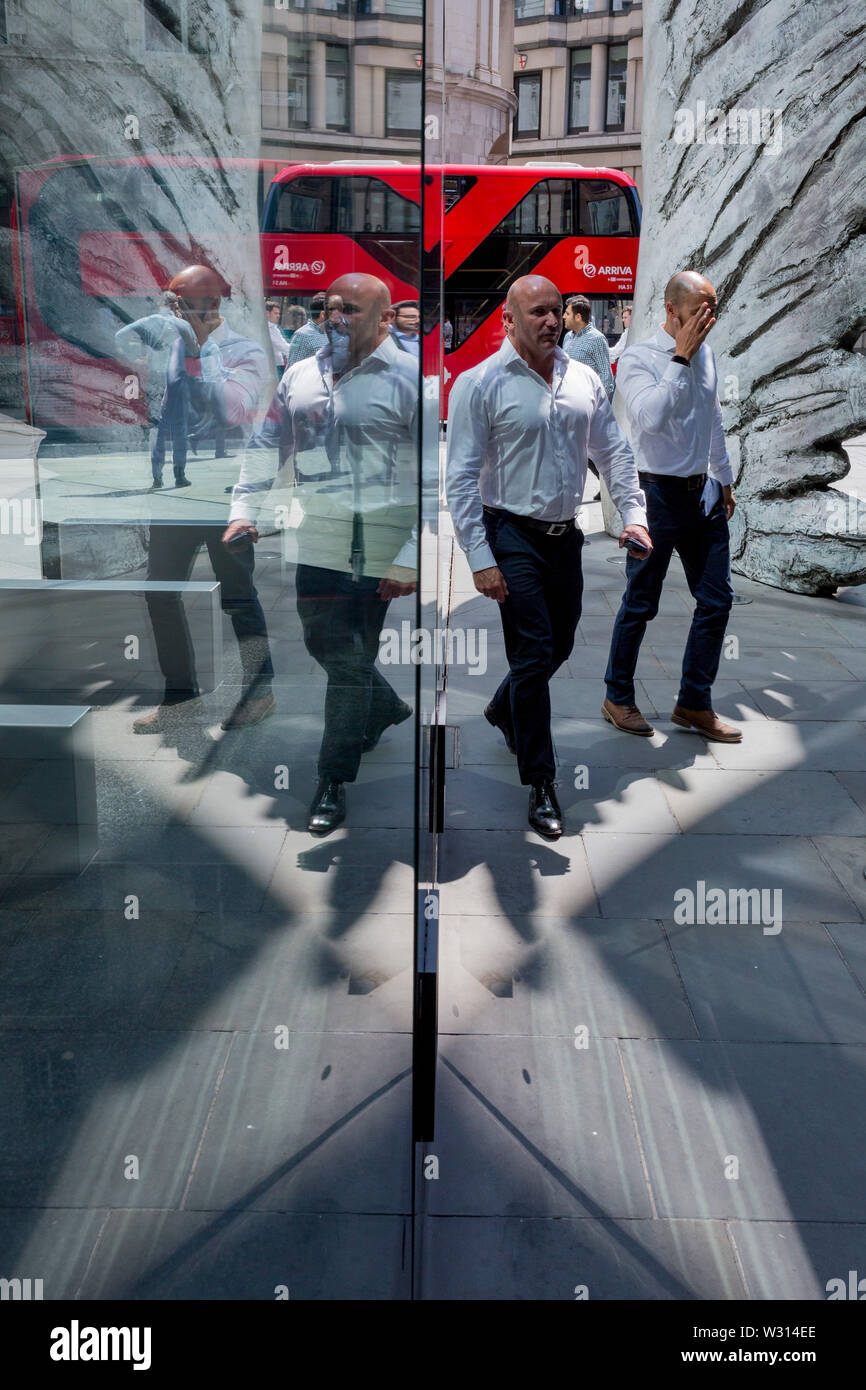 Les hommes d'affaires de l'industrie financière à pied au-delà de la sculpture intitulée City Wing sur Threadneedle Street dans la ville de Londres, le quartier financier de la capitale (aka le Square Mile), le 11 juillet 2019, à Londres, en Angleterre. L'aile est de la ville par l'artiste Christopher Le Brun. Les dix mètres de haut est la sculpture en bronze par le président de la Royal Academy of Arts, Christopher Le Brun, commandé par Hammerson en 2009. Elle est appelée 'La Ville' de l'aile et a été jeté par Morris Singer, fondateurs de l'art réputé pour être la plus ancienne fonderie d'art dans le monde. Banque D'Images