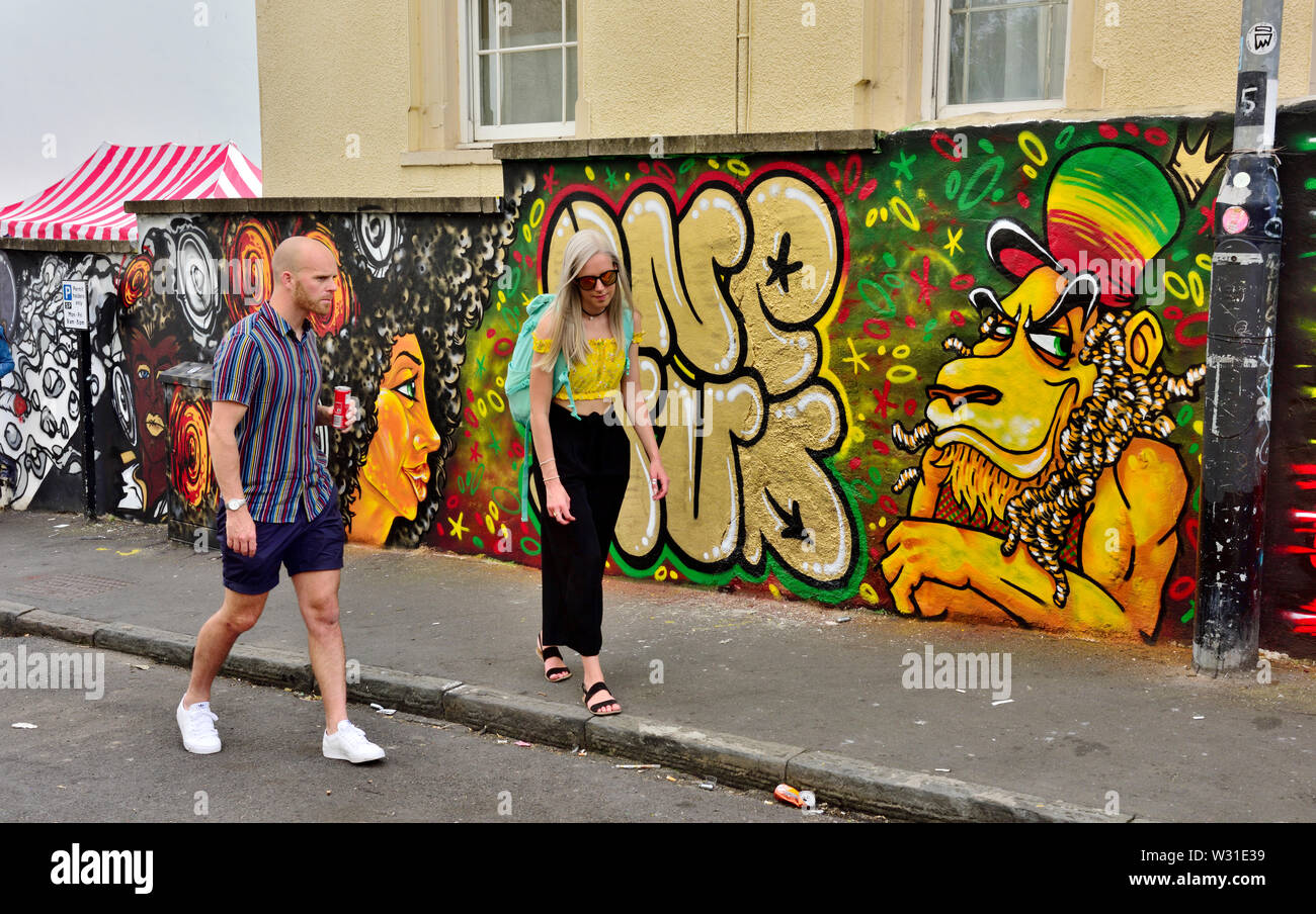 Deux personnes marchant le long de la route à St Paul's Bristol avec le street art derrière pendant le carnaval Banque D'Images
