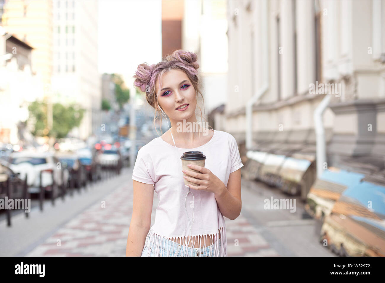 Smiling belle fille aux cheveux roses hairstyle marche dans la rue avec une tasse de café en carton bénéficiant d'une belle journée ensoleillée Banque D'Images