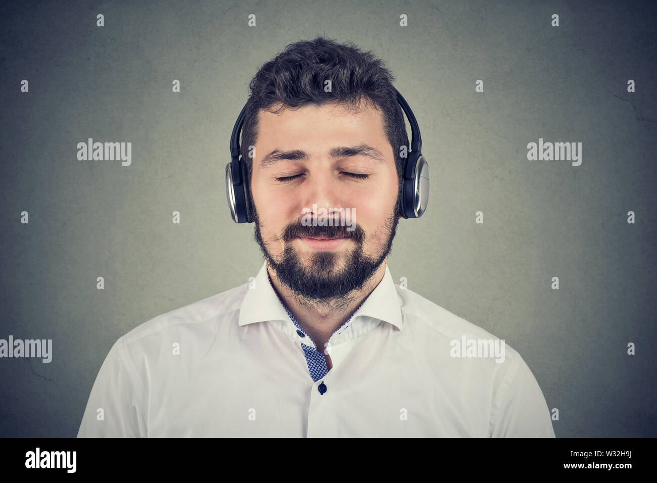 Beau jeune homme l'écoute de musique portant des écouteurs avec les yeux fermé sur fond gris Banque D'Images