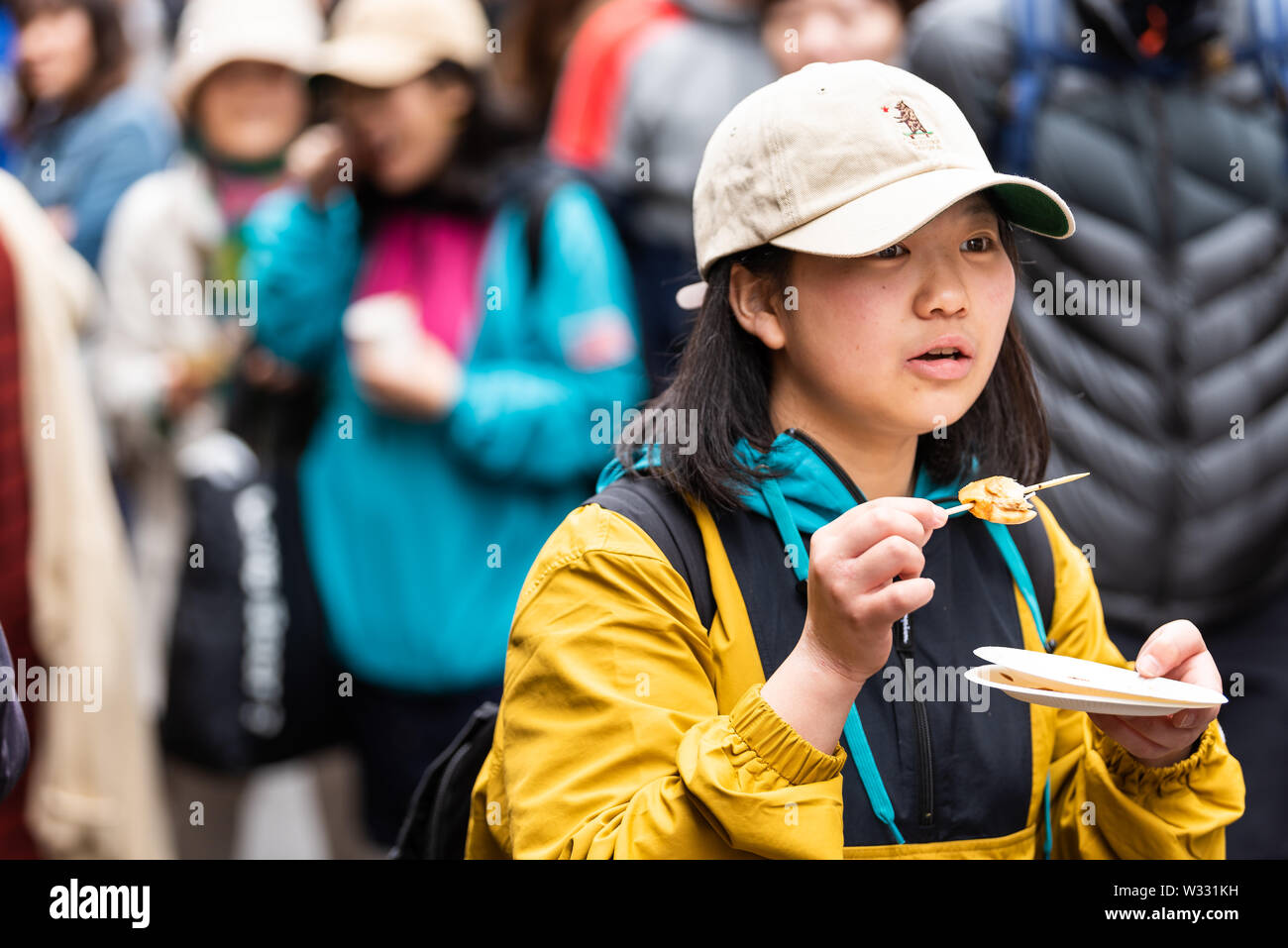 Tokyo, Japon - 30 mars 2019 : woman holding de touristes chinois de manger des fruits de mer brochette de poulet brochettes ou à Ginza rue Marché aux poissons Tsukiji extérieur avec Banque D'Images